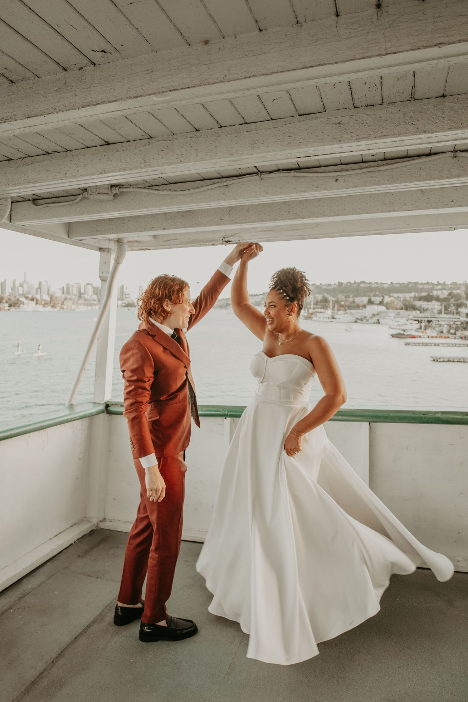 A joyful wedding dance moment on a boat deck with views of the water and skyline.