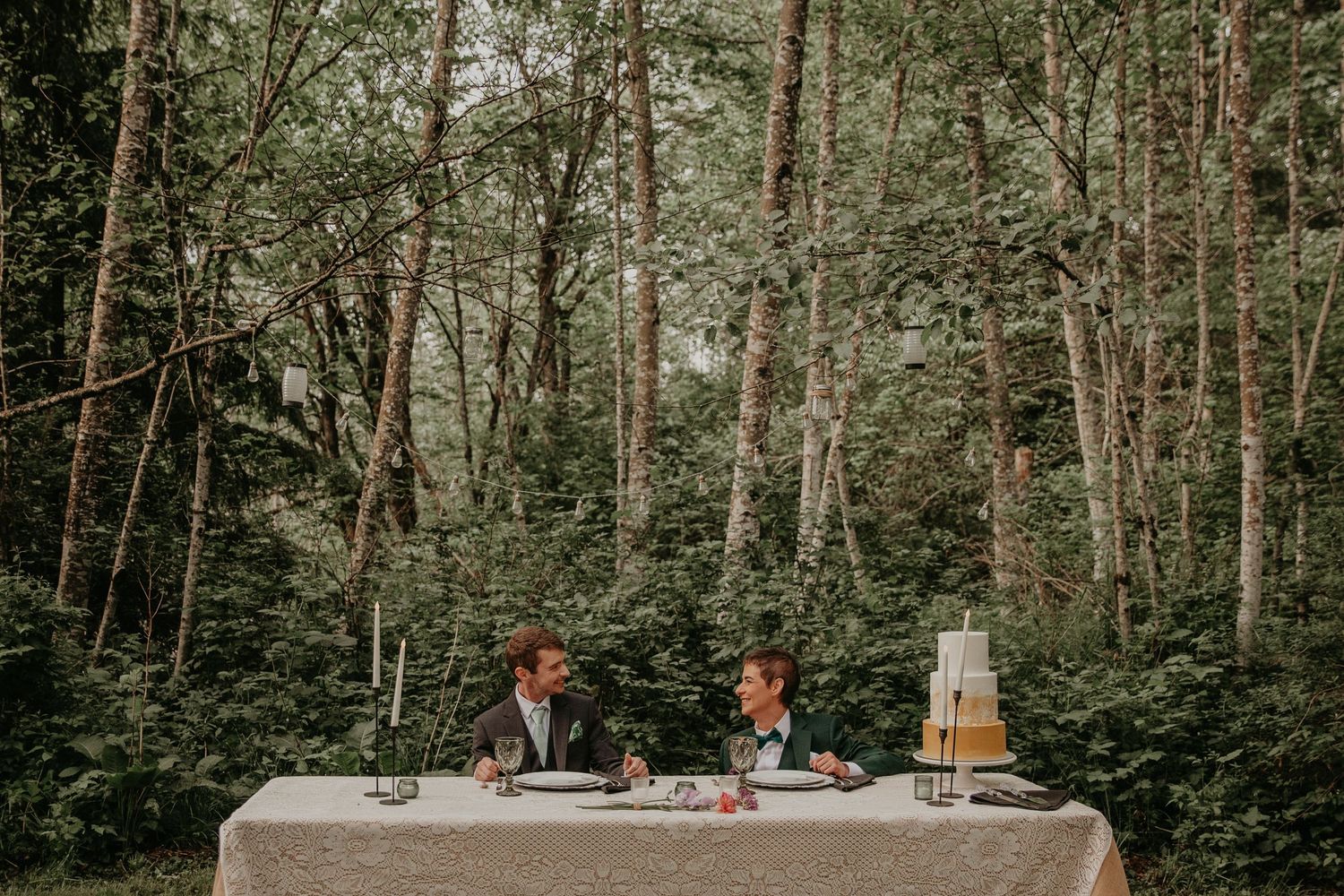 Two guests dine at an elegant table in the woods with tall trees creating a natural forest backdrop.