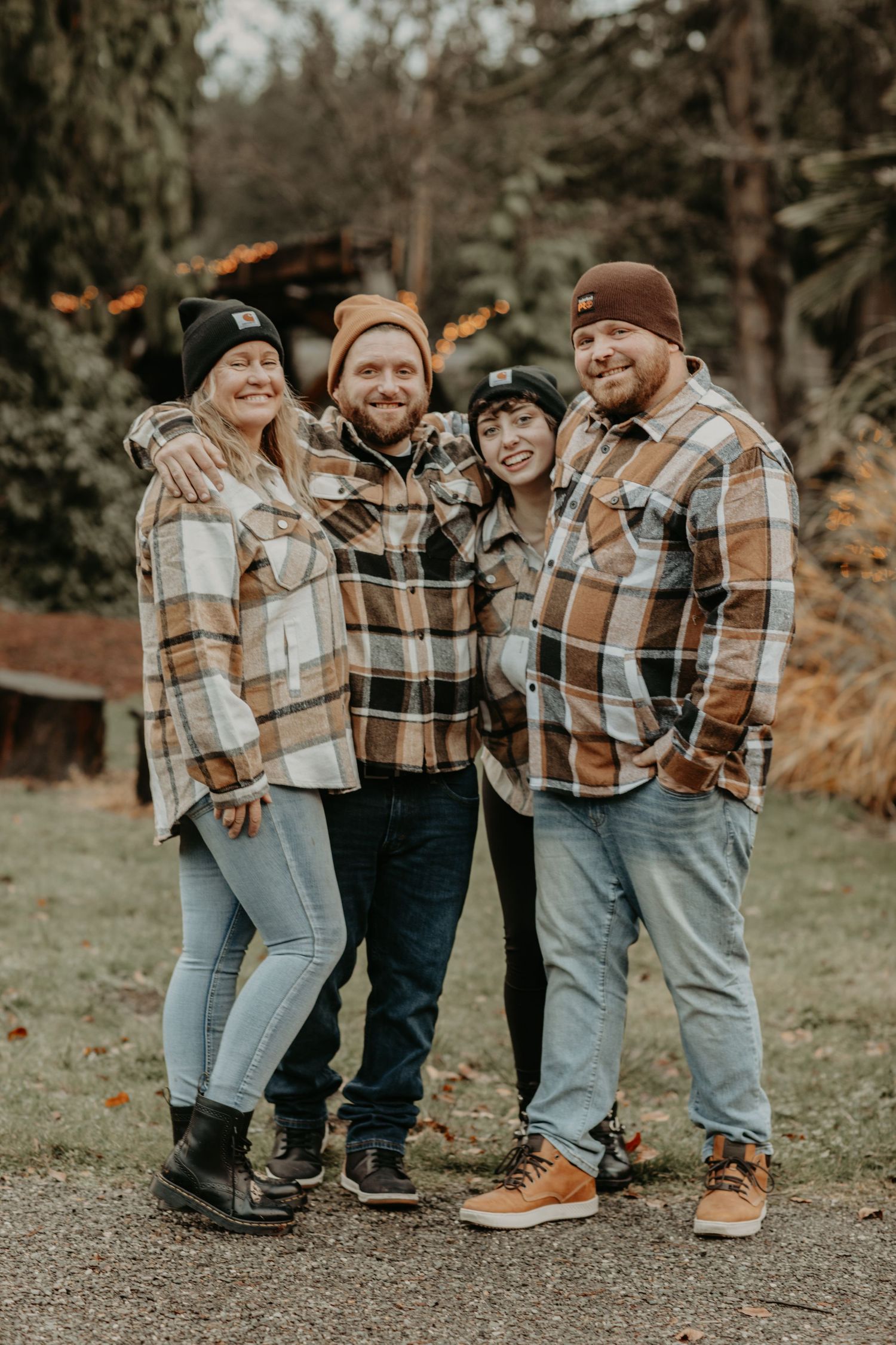 Four people wearing matching plaid flannel jackets and beanies pose together outdoors on an autumn day.