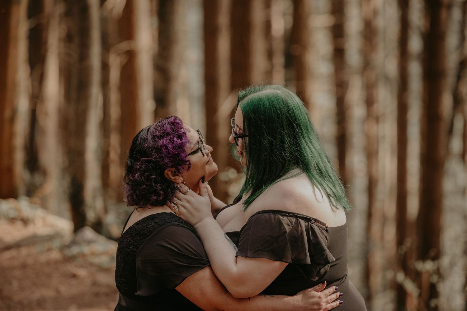 Two people with dyed hair share an intimate moment together in a sunlit forest setting during golden hour.