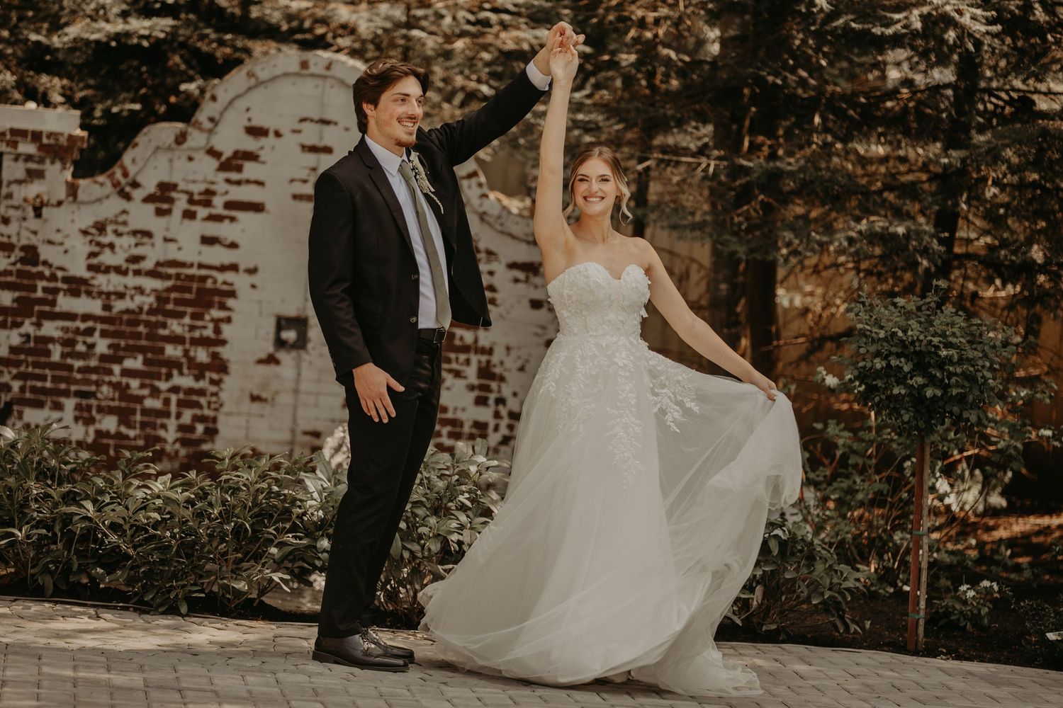 A romantic autumn wedding photo showing a couple posing against rustic brick walls in formal attire.