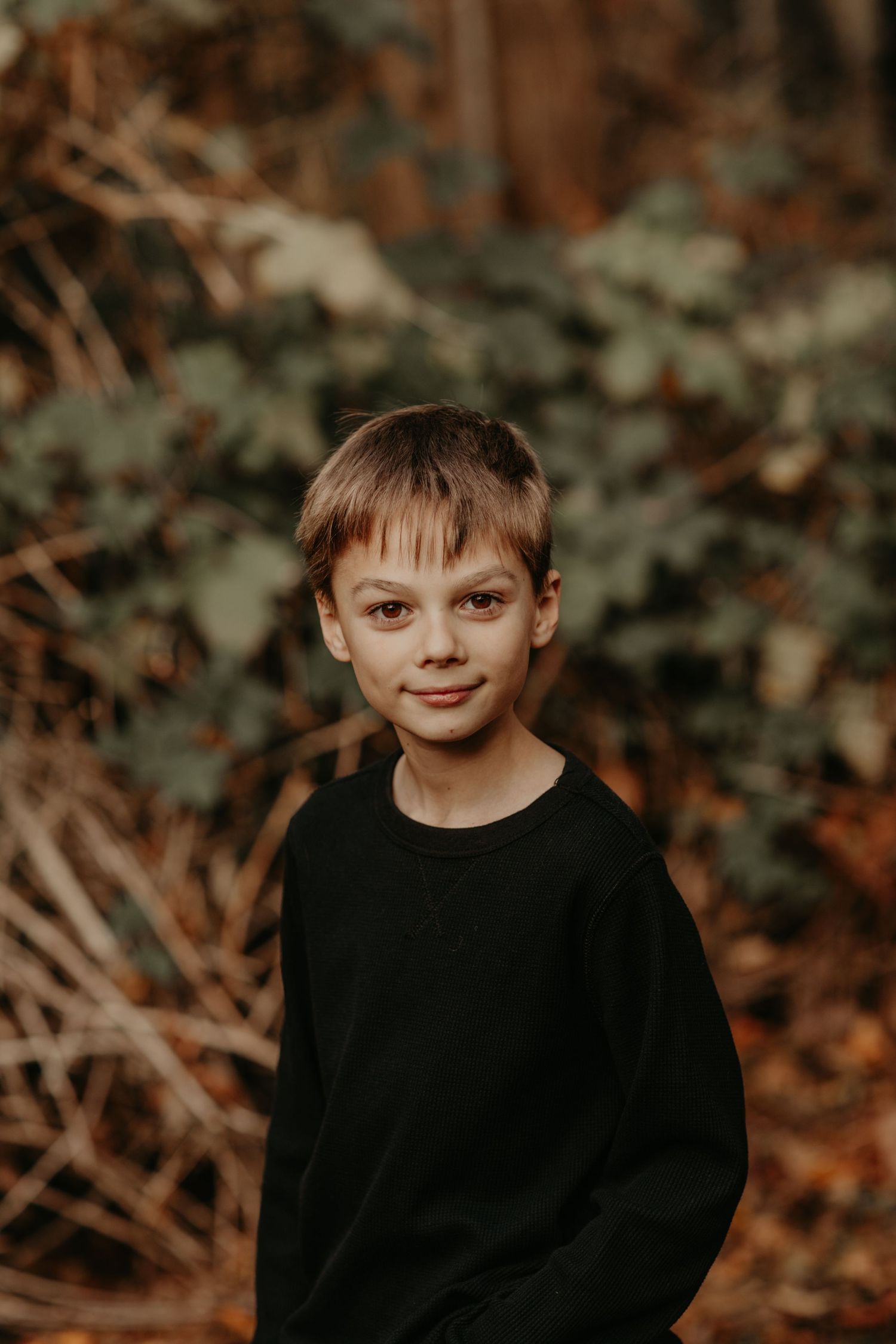 Portrait of a young person wearing a black sweater against a blurry natural outdoor background with autumn colors.