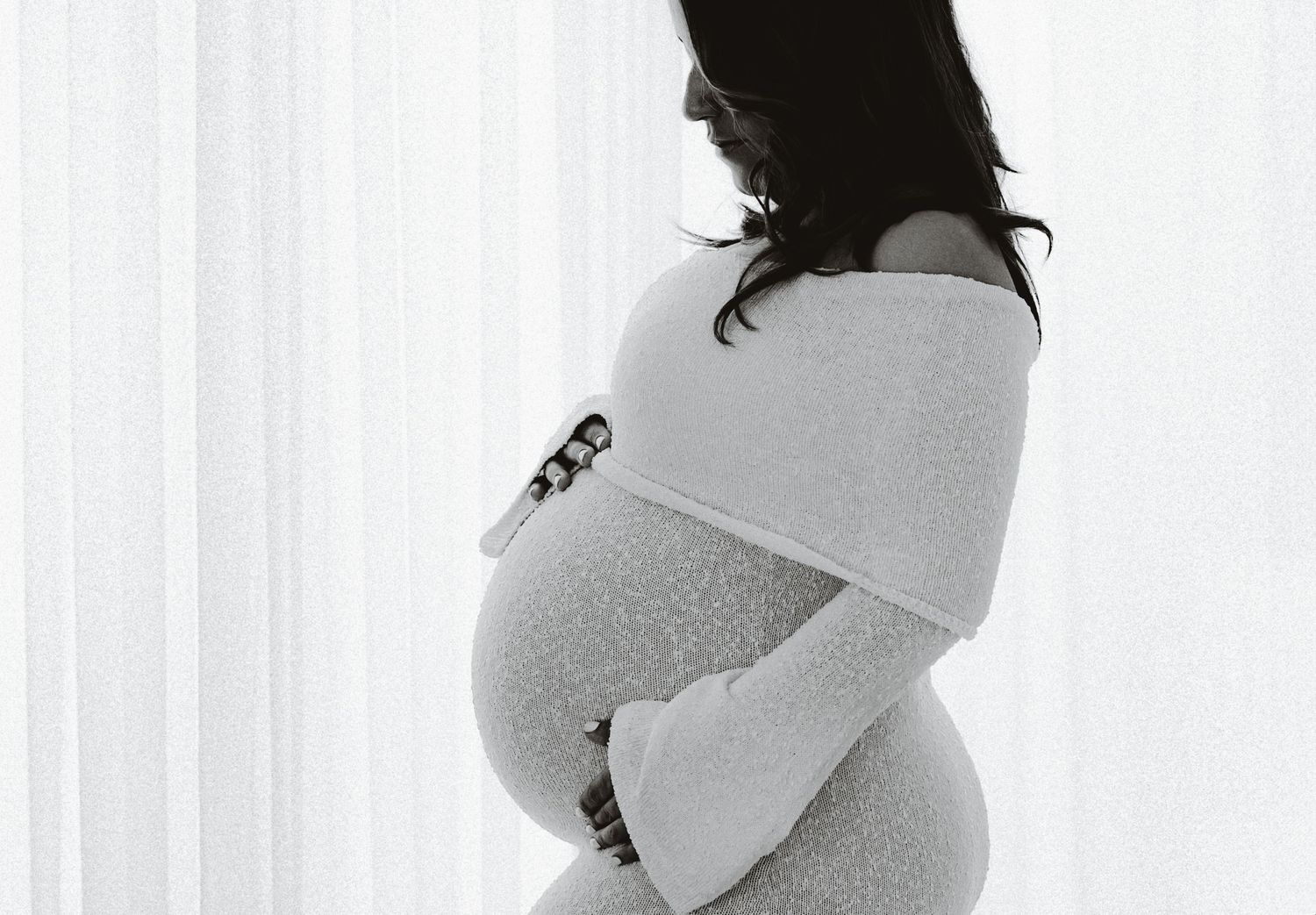 Silhouette maternity photo showing expecting mother in cozy wrap against window light.