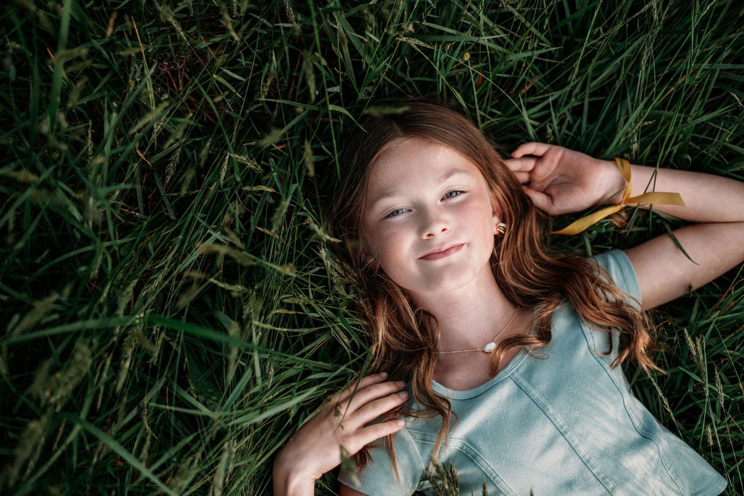 Top view portrait of someone lying in tall green grass on a sunny day.