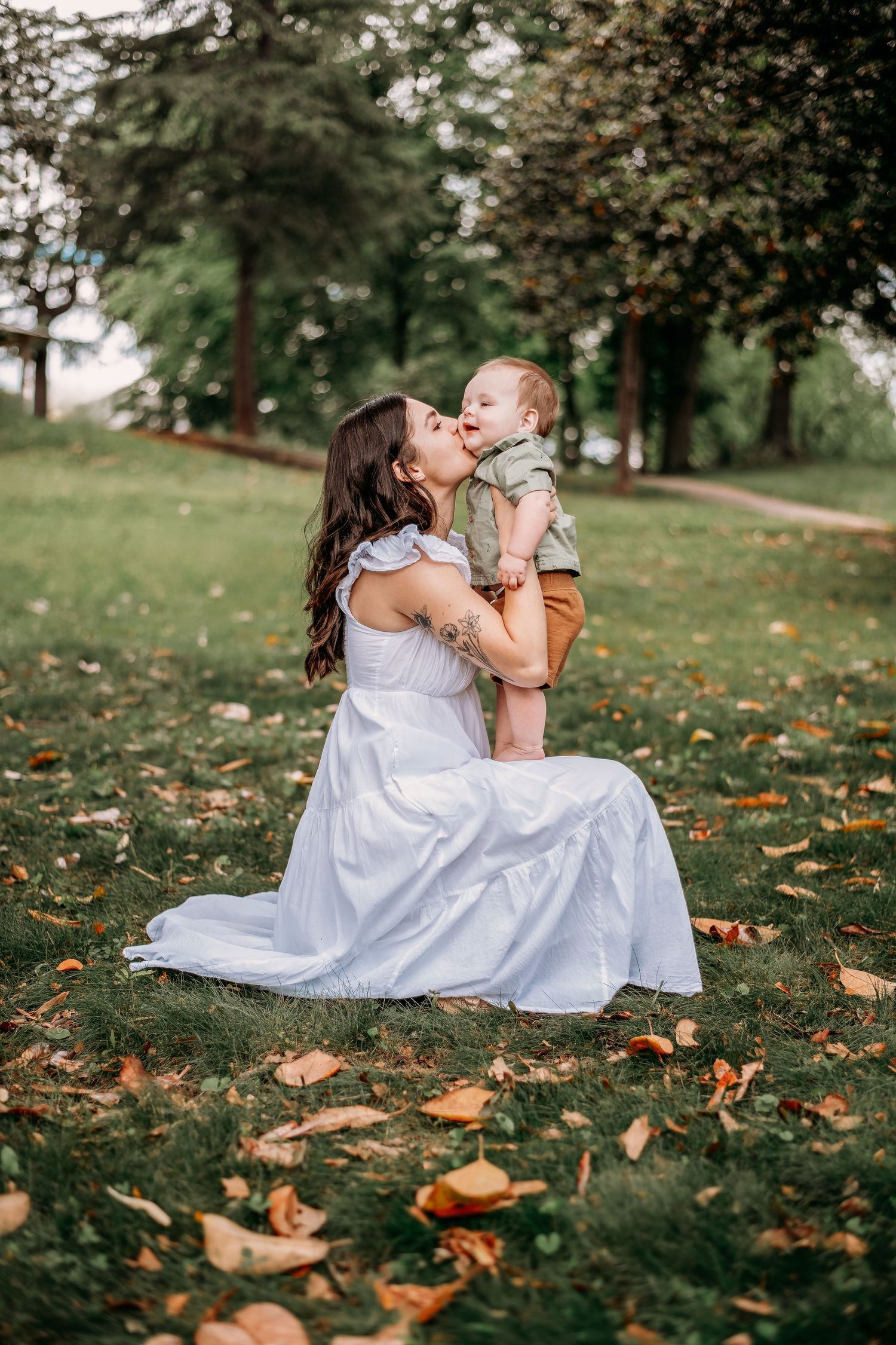 A tender outdoor autumn portrait with fallen leaves scattered on grassy ground.