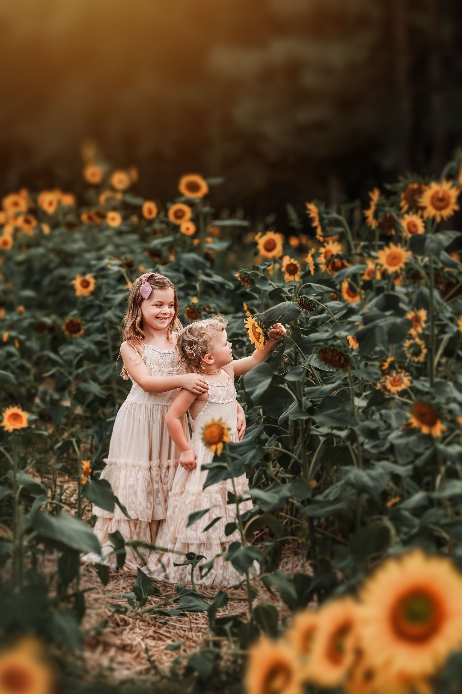 Siblings stand together among blooming sunflowers in a dreamy summer garden setting at golden hour.