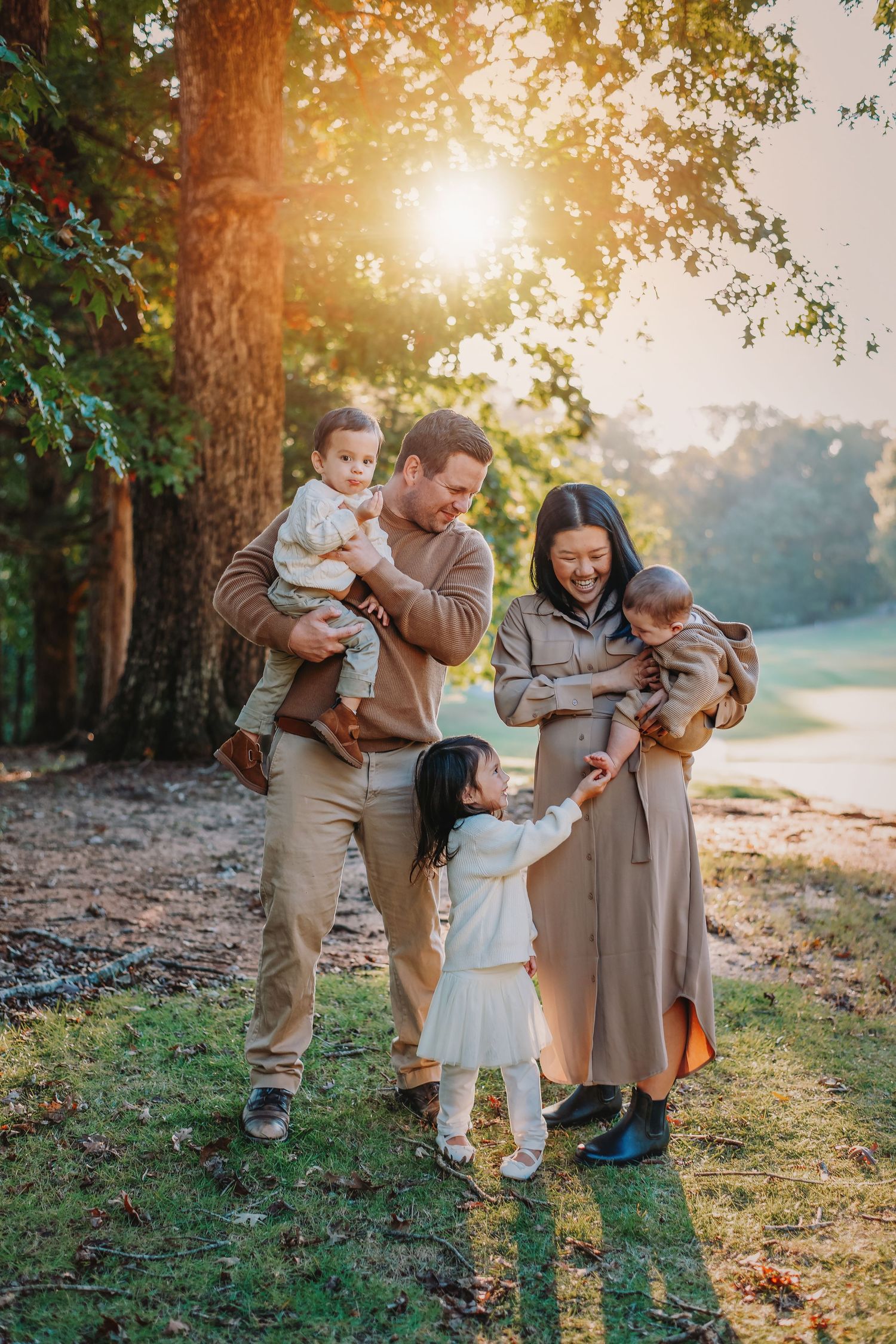 Family enjoys playful moment together in sunlit forest setting.