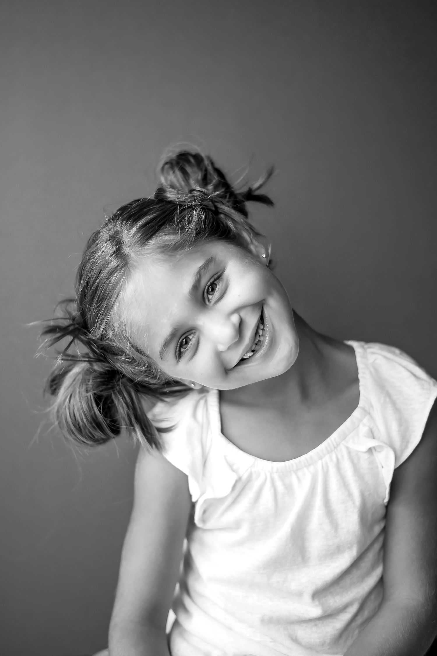 Black and white portrait of child with pigtails smiling brightly.