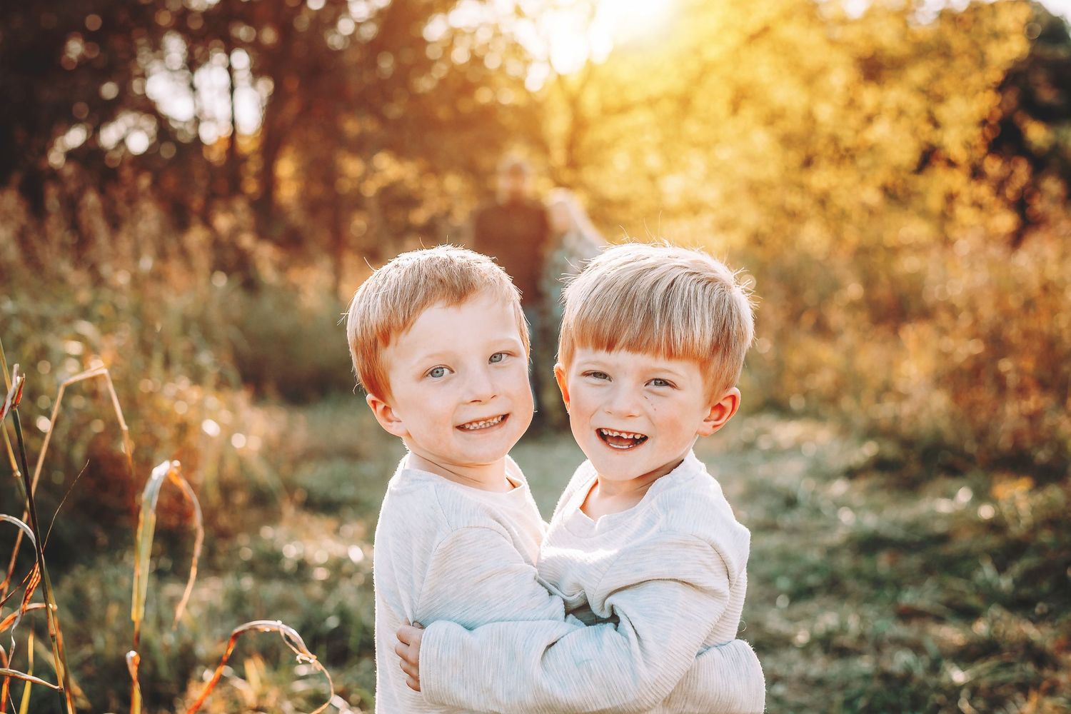 Two children sharing joyful laughter together in golden sunlit field at sunset.