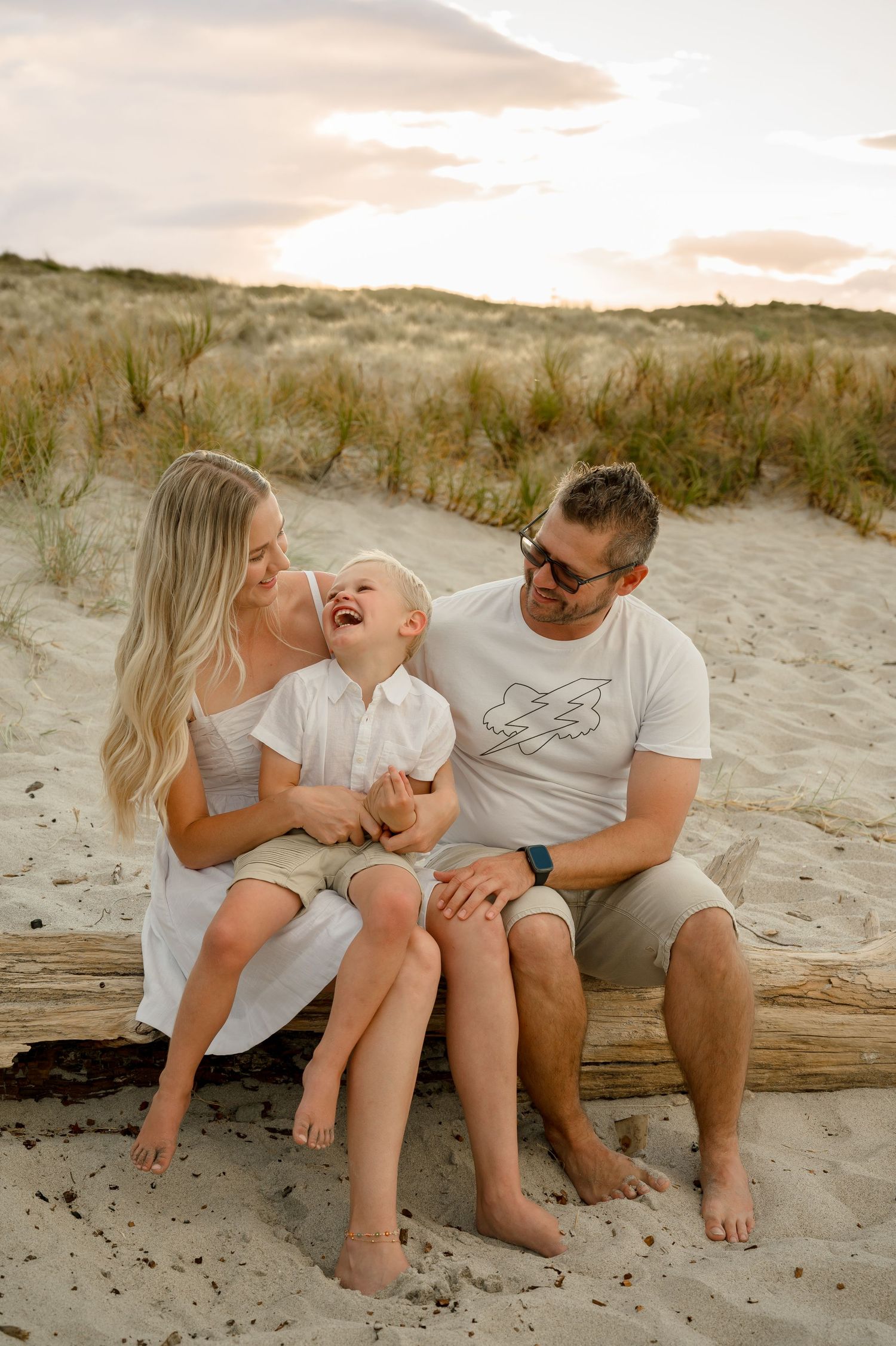 A family shares a joyful moment together while sitting on driftwood at the beach during sunset.