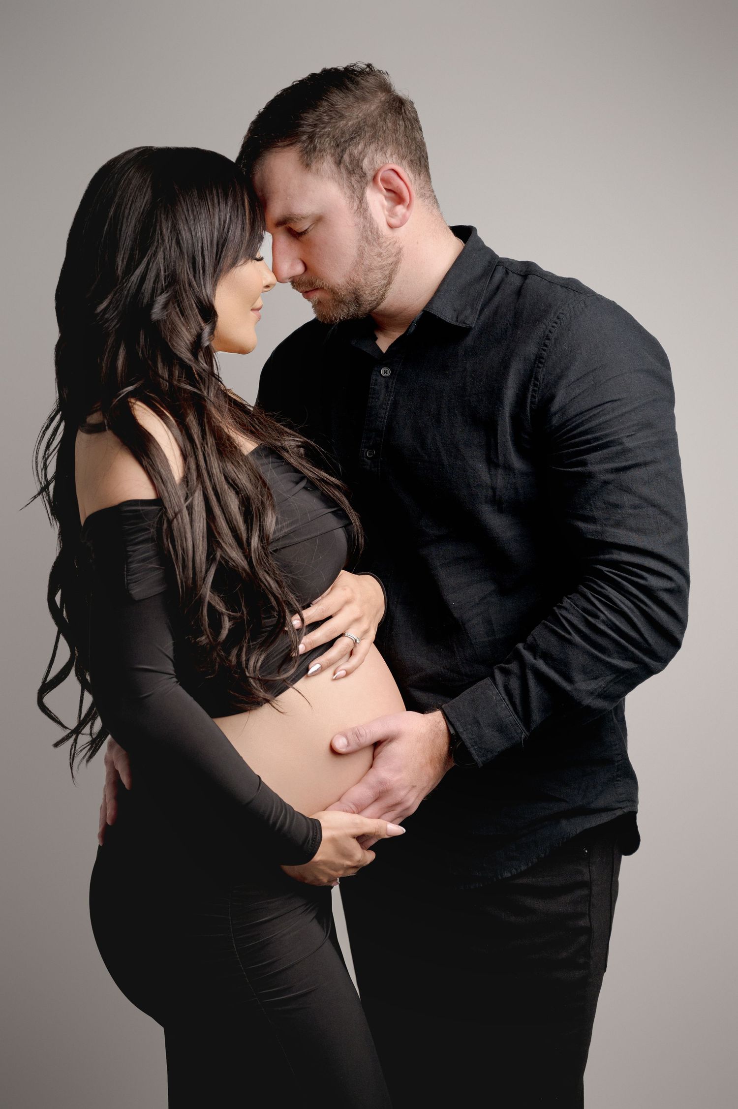 Romantic maternity portrait of couple in black attire sharing intimate moment.