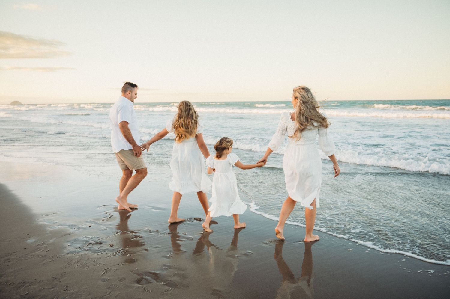 People in white clothing dance together at the beach during sunset as ocean waves roll onto the shore.
