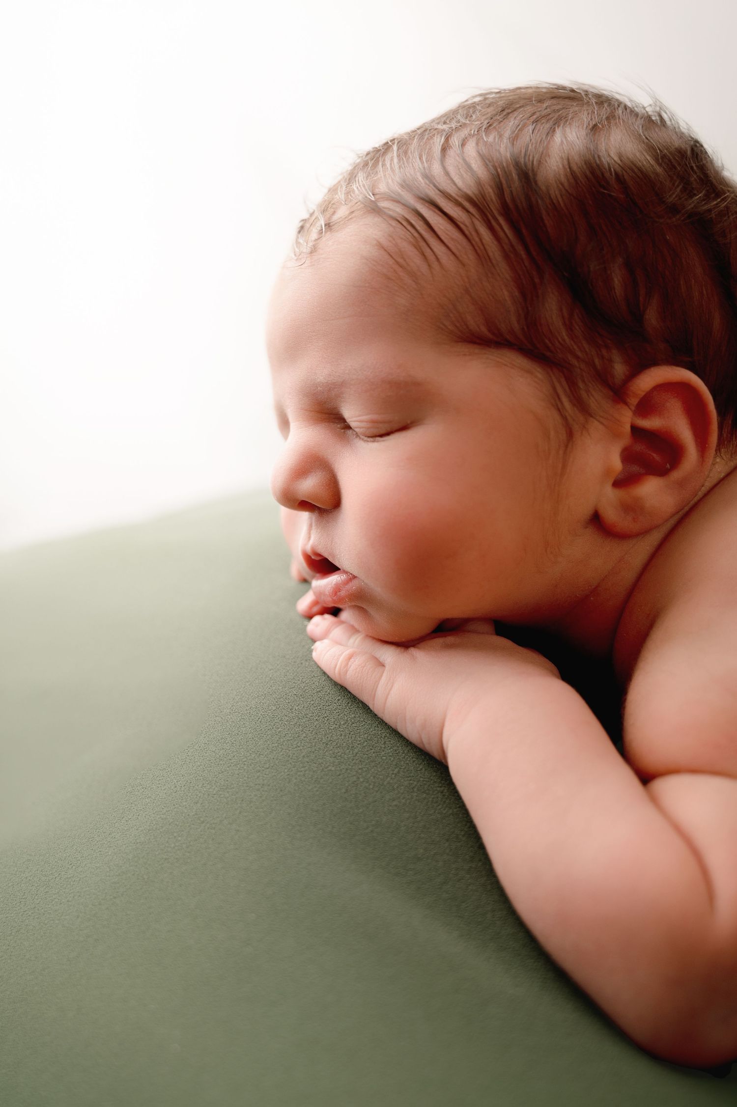 Peaceful sleeping newborn baby lying on soft sage green bedding in natural light.