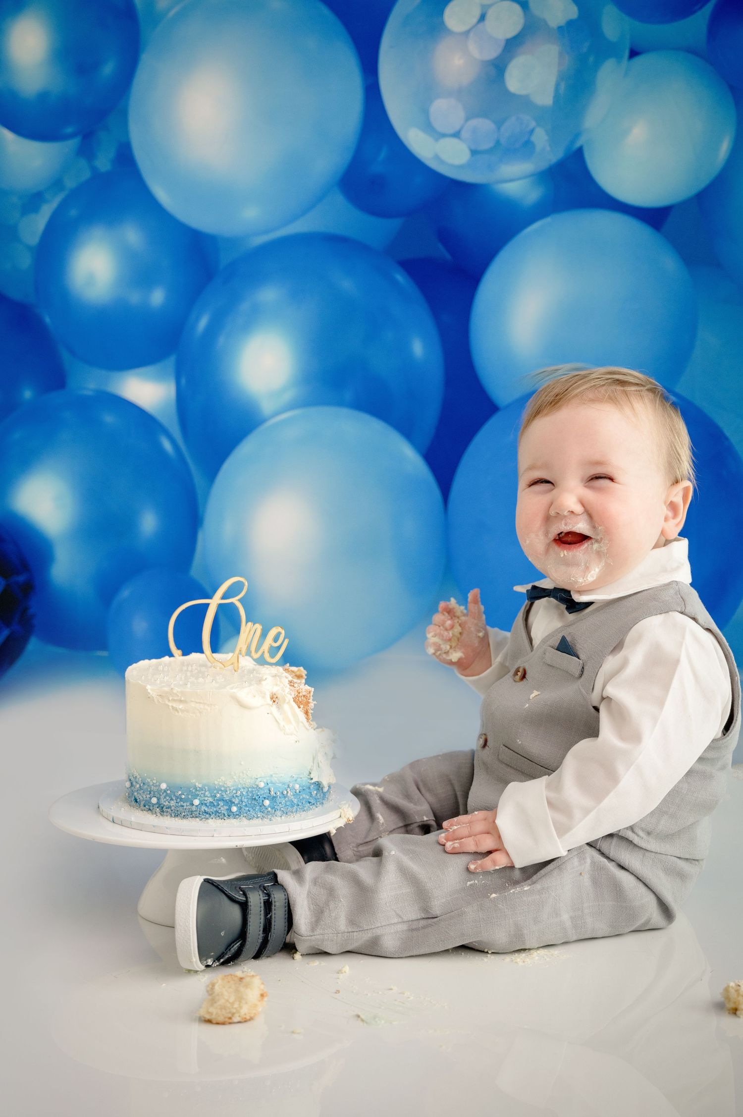 A cake smash photo setup with blue balloon background and small cake on white pedestal.