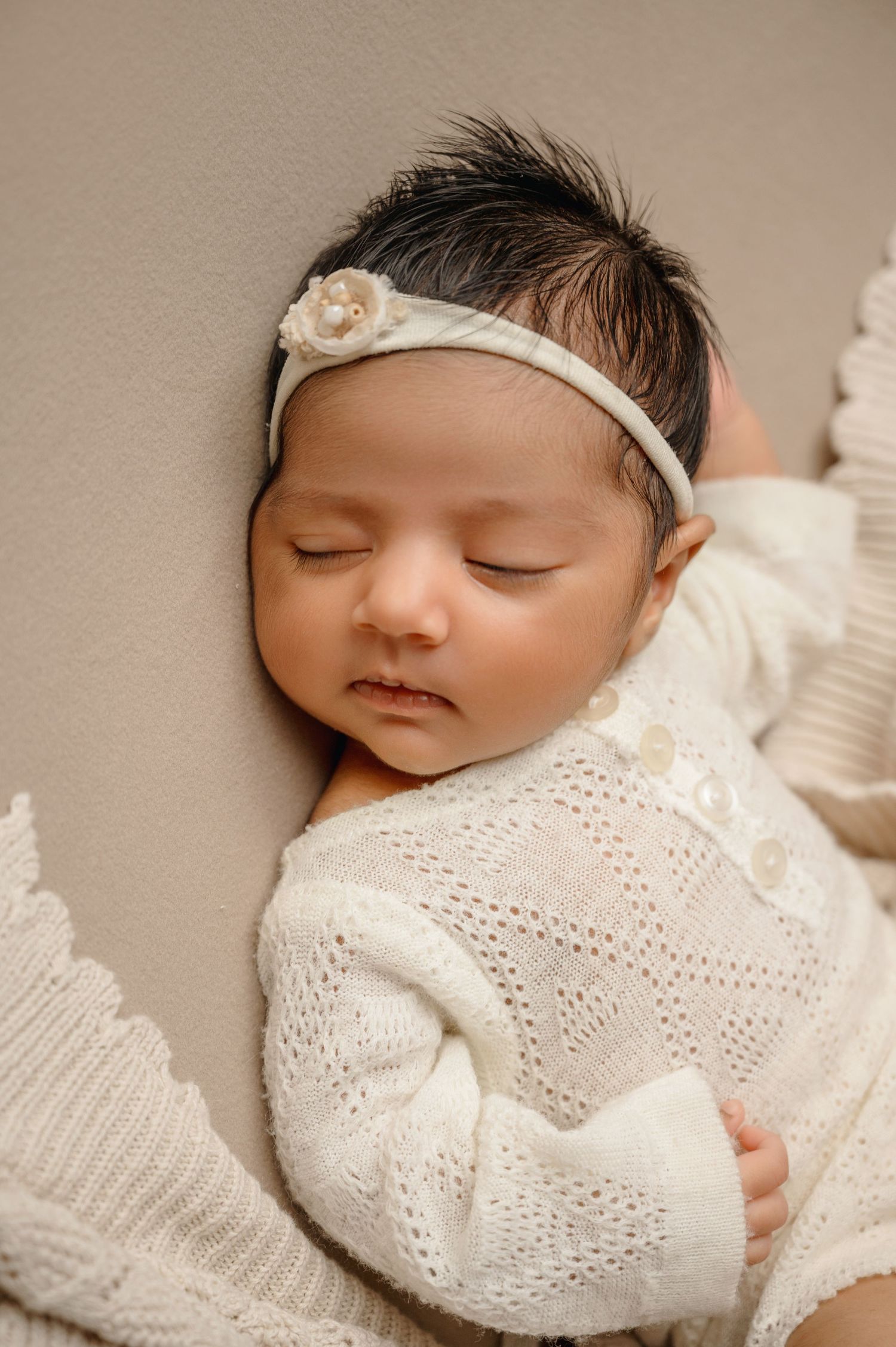 Peaceful newborn wearing a delicate white headband and knit outfit while sleeping.