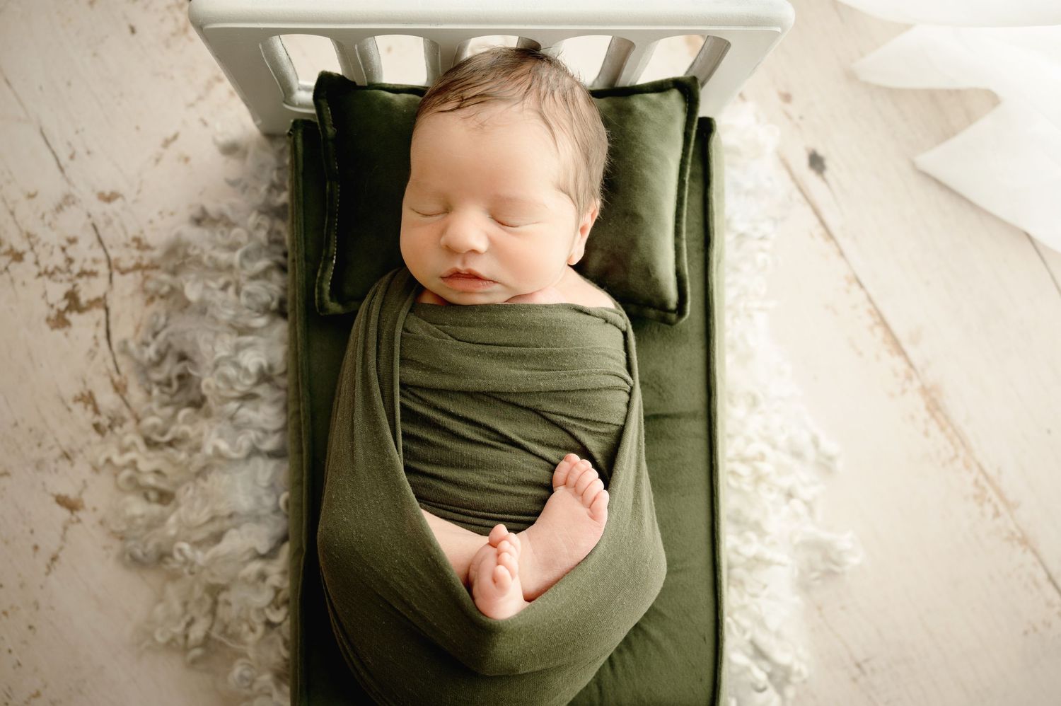 A series of photographs showing a swaddled infant against green fabric with warm neutral backgrounds.
