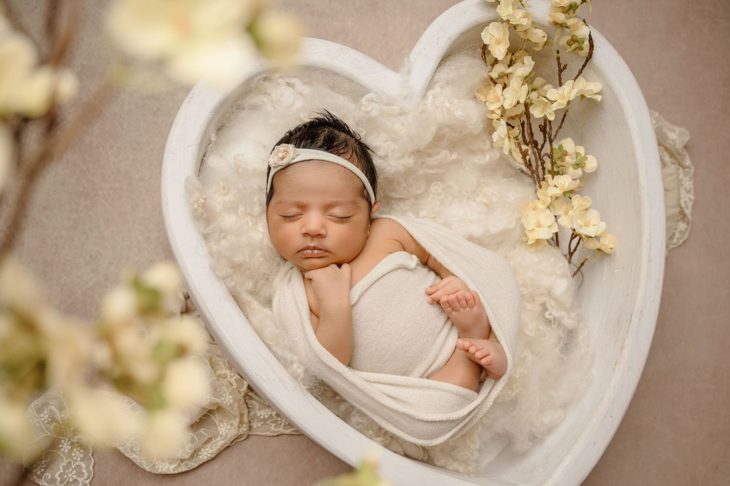 Peaceful newborn photography in heart-shaped prop with gold floral accents.