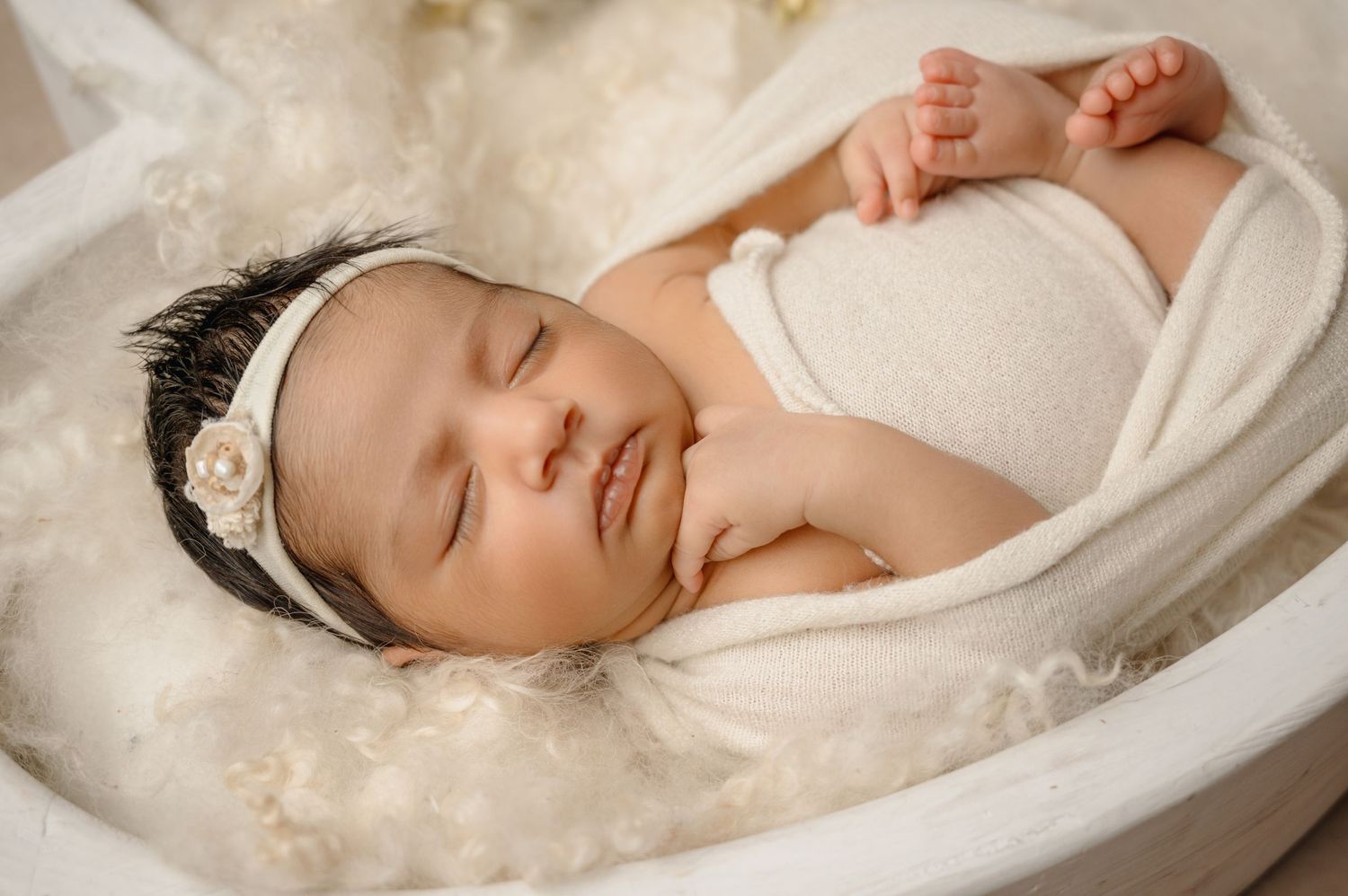Peaceful sleeping newborn in white on soft cream-colored bedding.