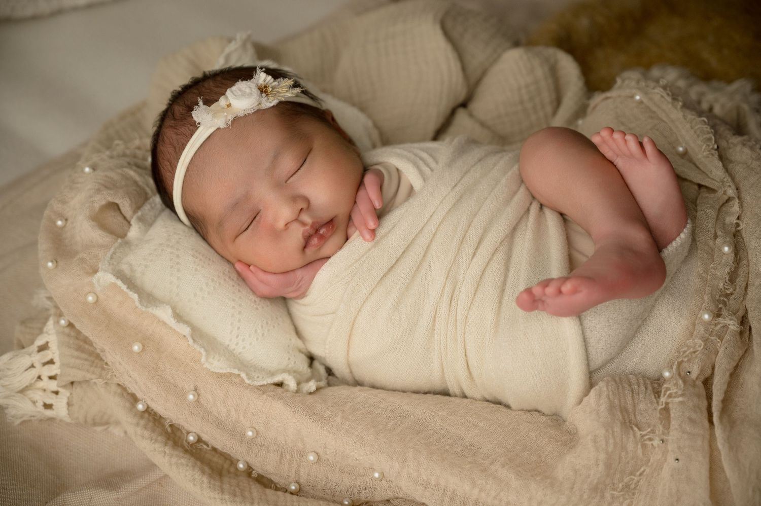 Four sequential photos showing a sleeping newborn baby swaddled in cream-colored fabric against a textured background.