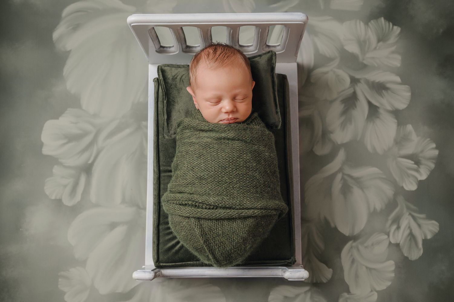 A set of artistic newborn photography portraits showing sleeping baby wrapped in green blanket against soft gray floral backdrop.