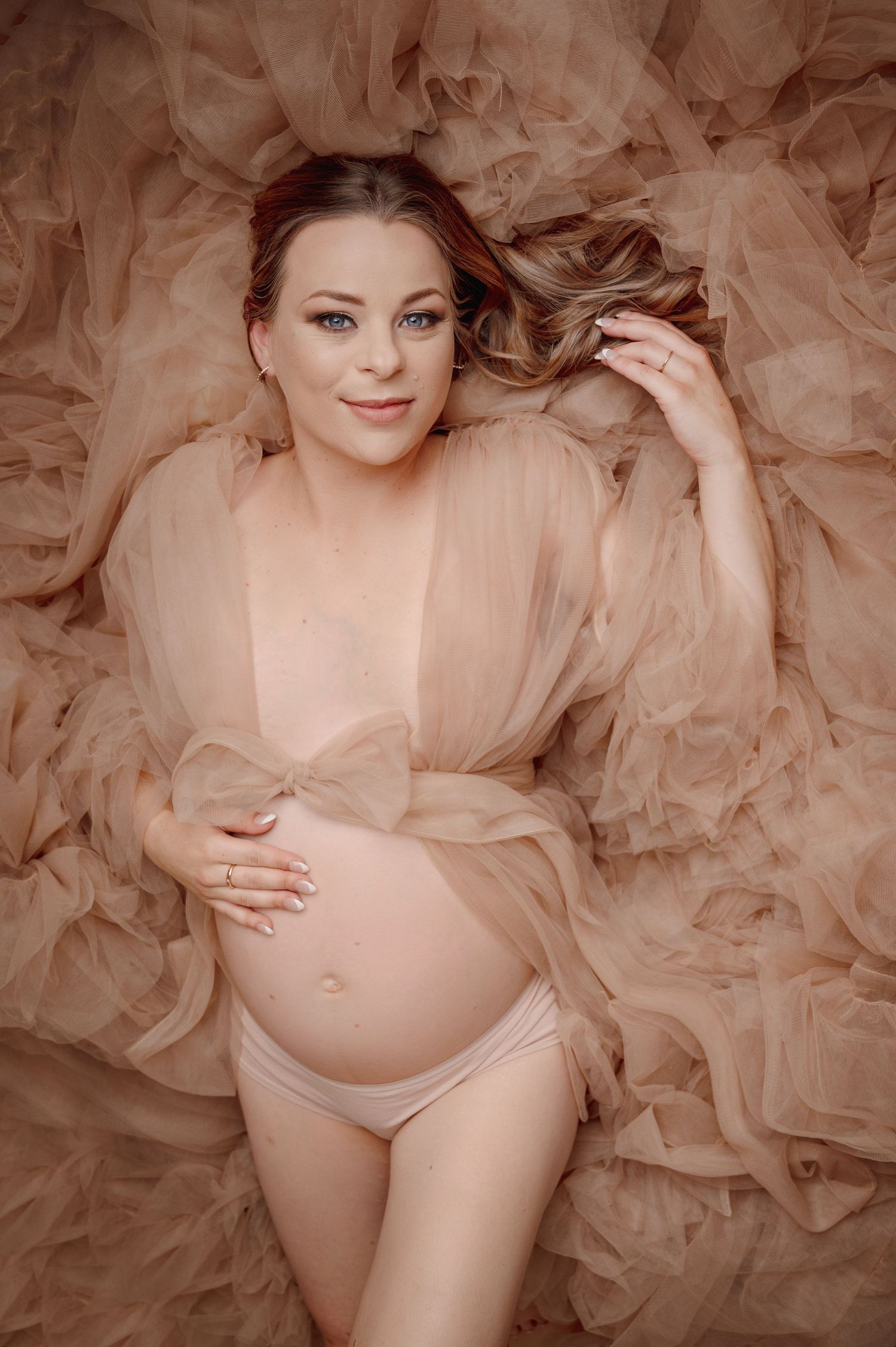 Dreamy maternity boudoir photo with flowing peach tulle fabric and soft romantic lighting.