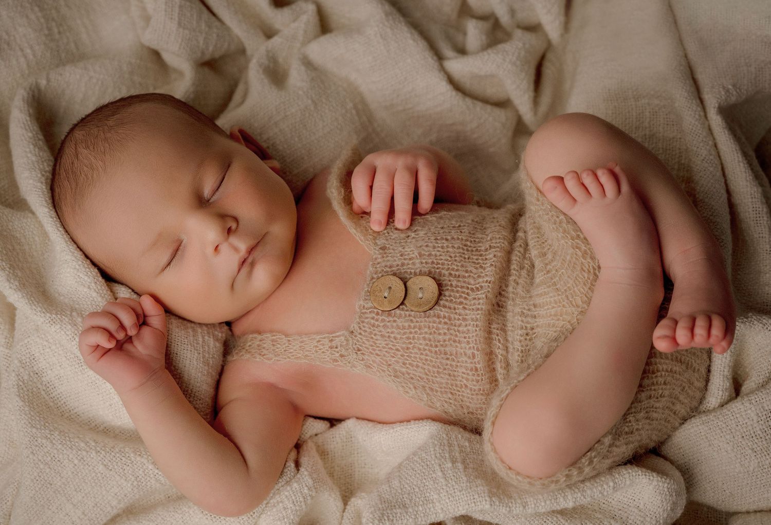 A series of peaceful newborn baby photographs showing sleeping infants swaddled in soft beige blankets.
