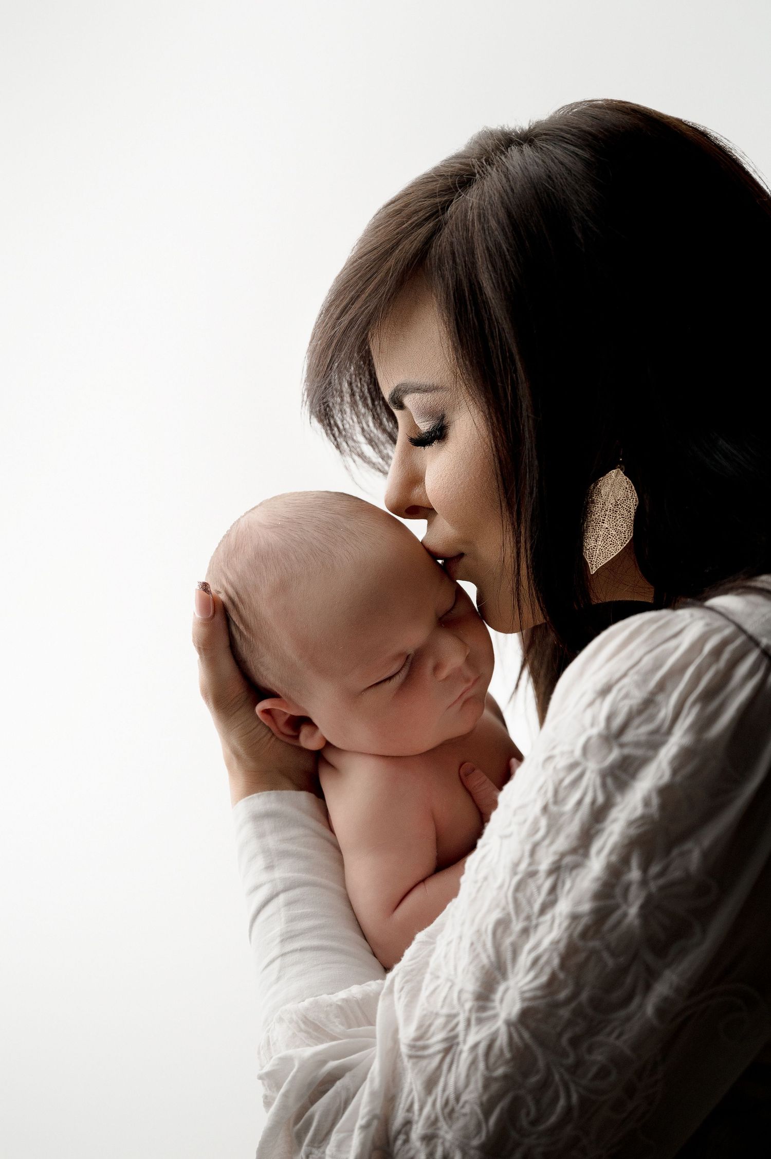 Tender moment between parent and newborn baby in soft white lighting with cozy cable knit sweater.