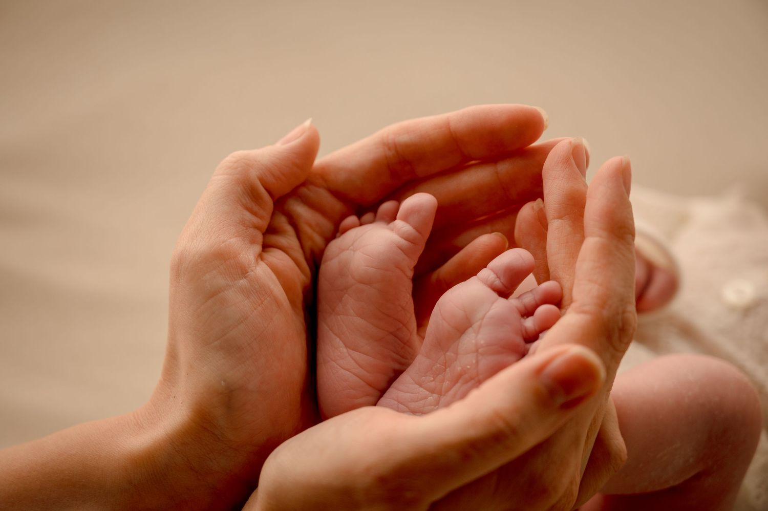 A tiny baby foot nestled between caring adult hands in a tender moment of bonding.
