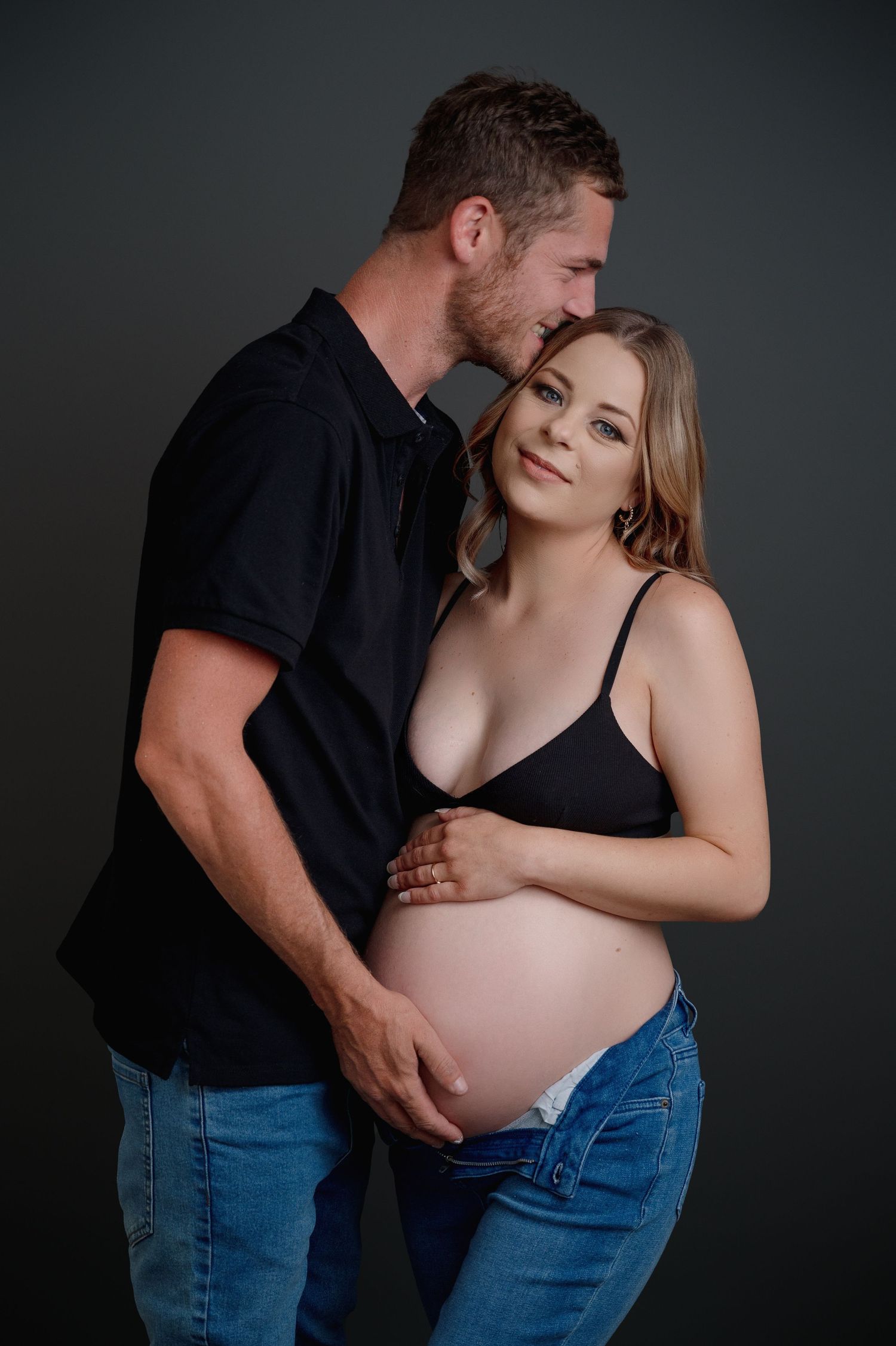 A maternity photo series showing intimate moments between partners against a dark backdrop with dramatic lighting.