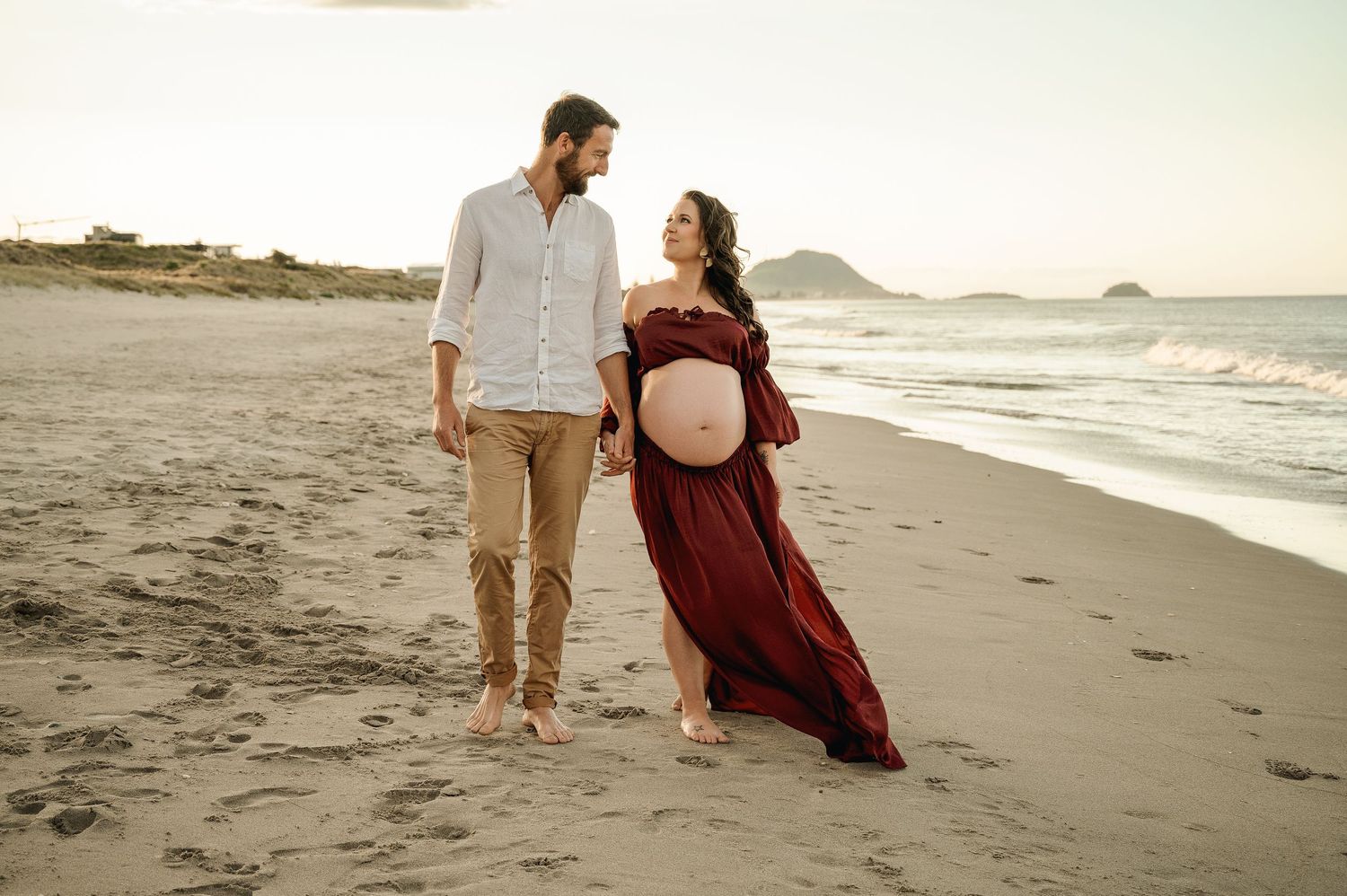 Couple in casual attire sharing intimate moments while walking along a scenic beach at sunset.