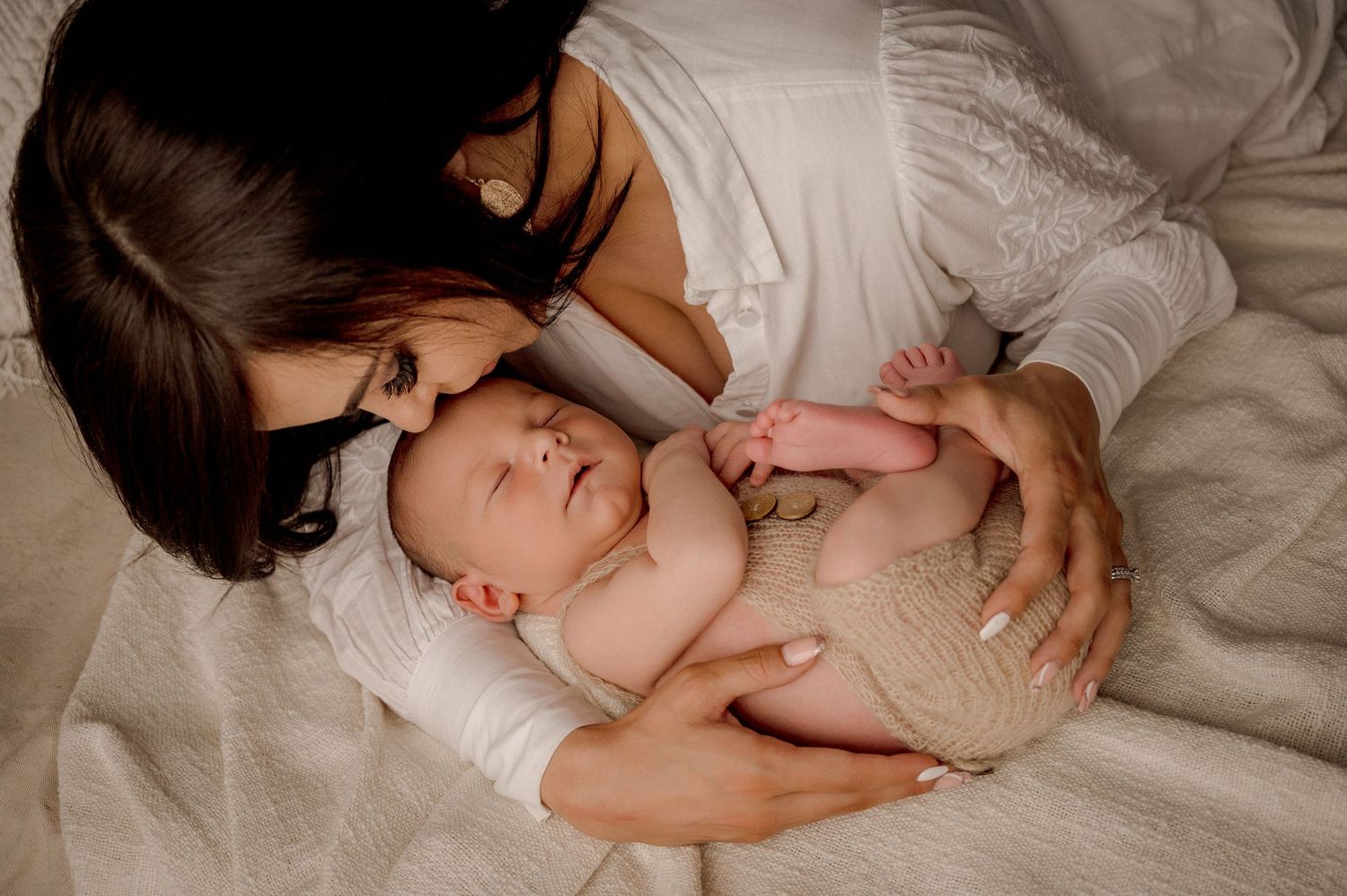 A tender moment as a caregiver holds and interacts with a peaceful newborn baby on soft white bedding.