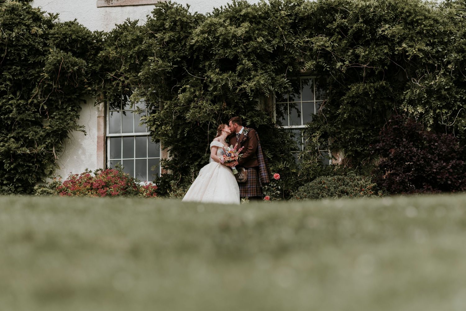 Scenic outdoor wedding venue with lush greenery and a white building in the background.
