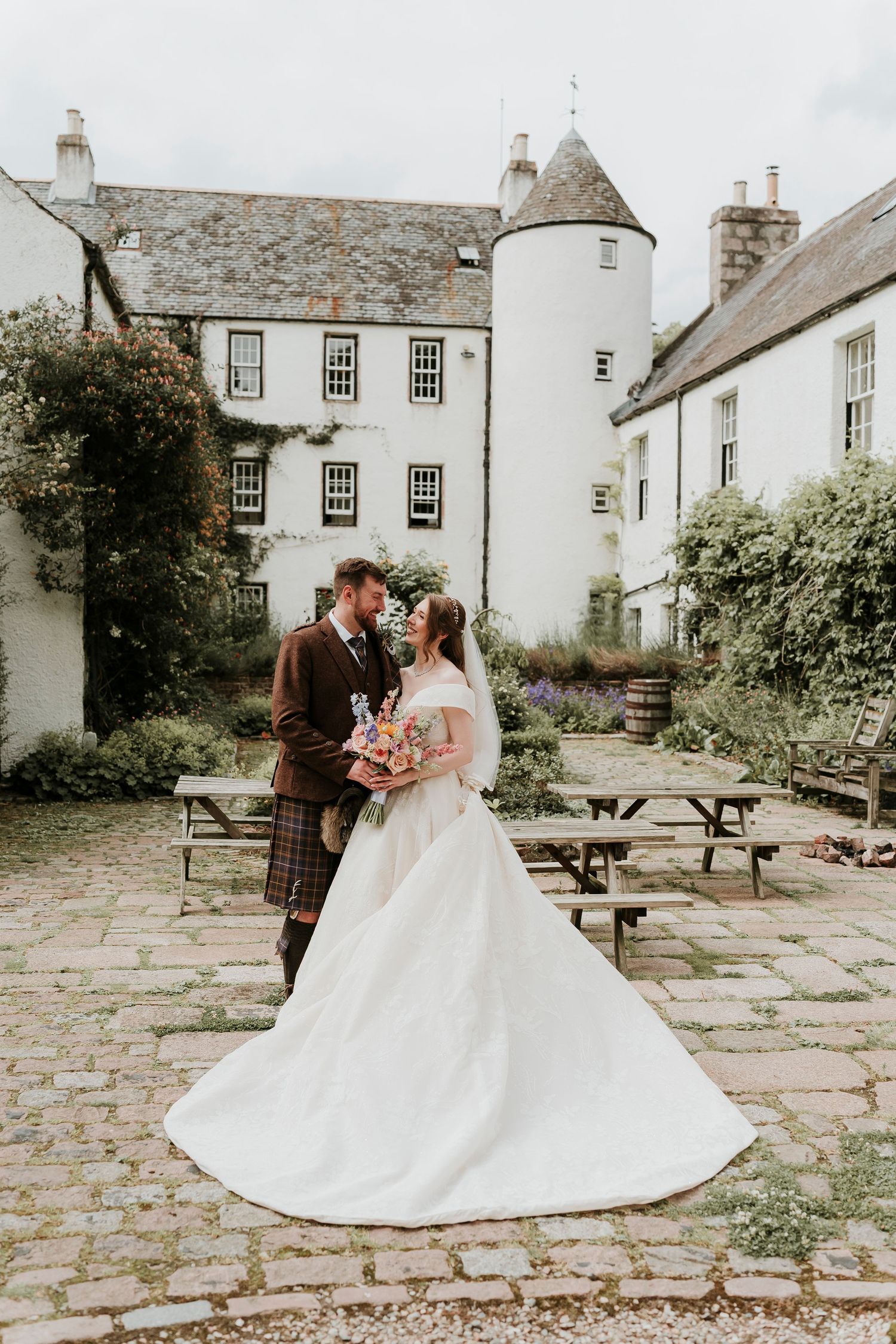 A wedding couple shares intimate moments on a stone patio courtyard surrounded by historic white buildings.
