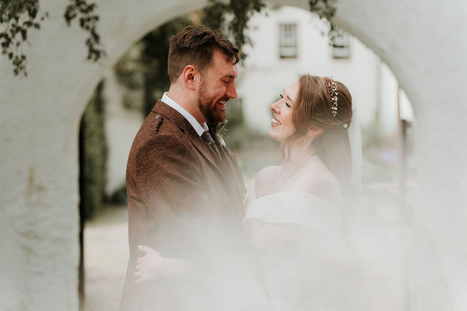 A romantic wedding photo captured through an arched passageway with a soft dreamy glow.