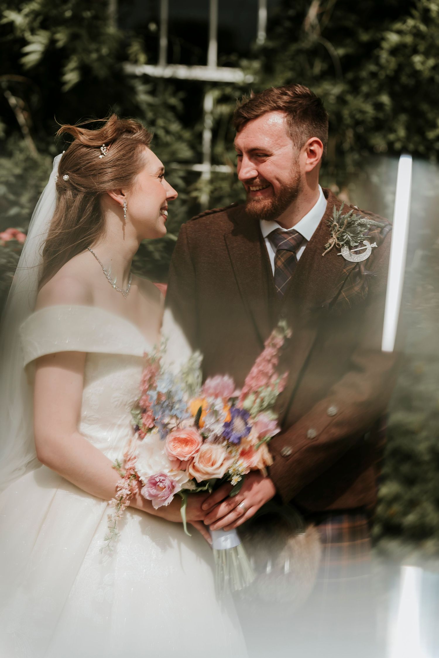 A romantic wedding moment in a garden setting with the couple holding a colorful floral bouquet.