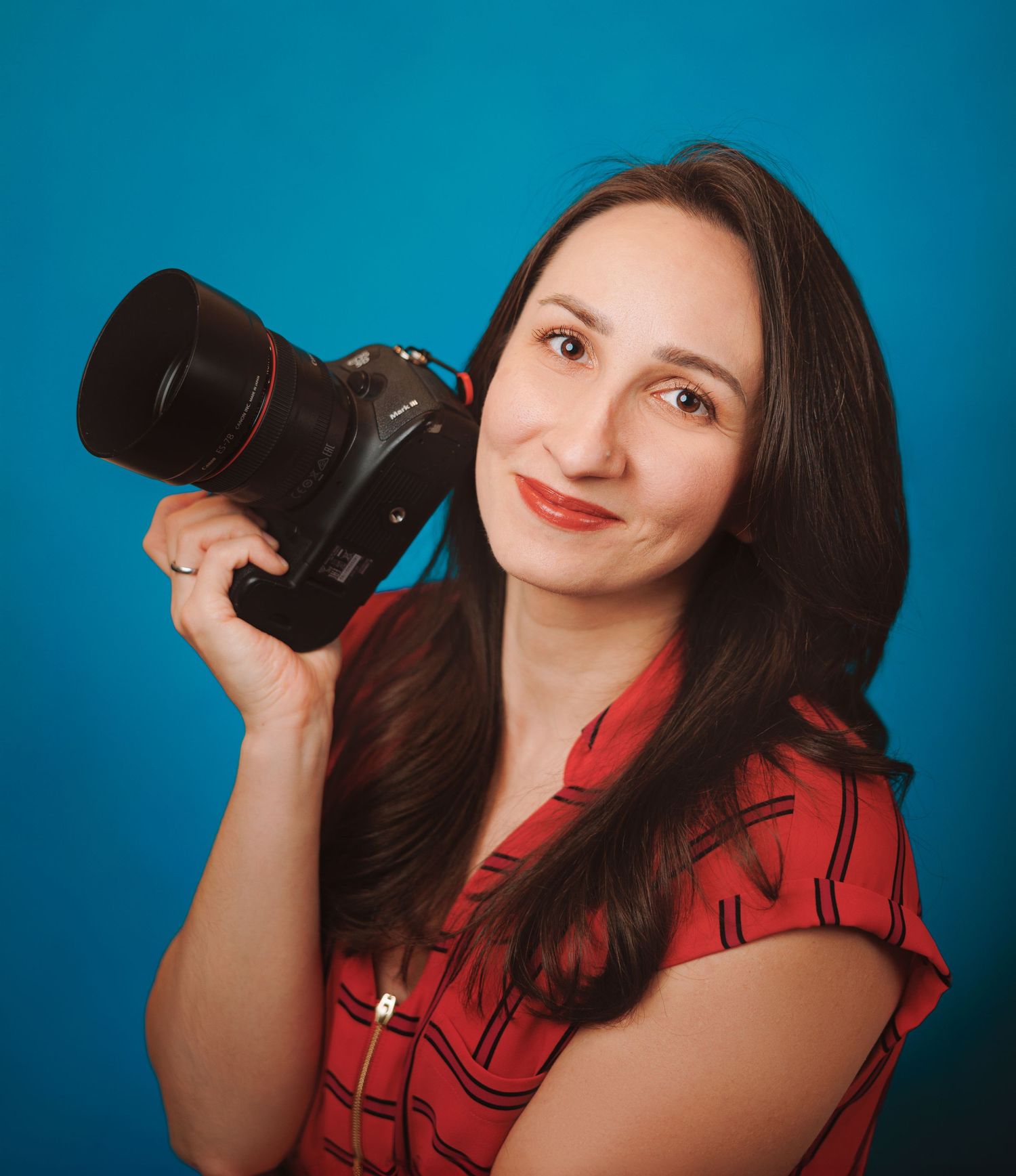 Caroline Spiz is smiling holding her camera against a blue backdrop