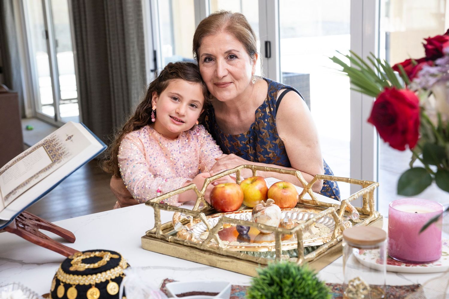 Family gathering around a wooden table with fresh fruit, sweets, and homemade treats on a decorative gold tray. Grandmother portrait