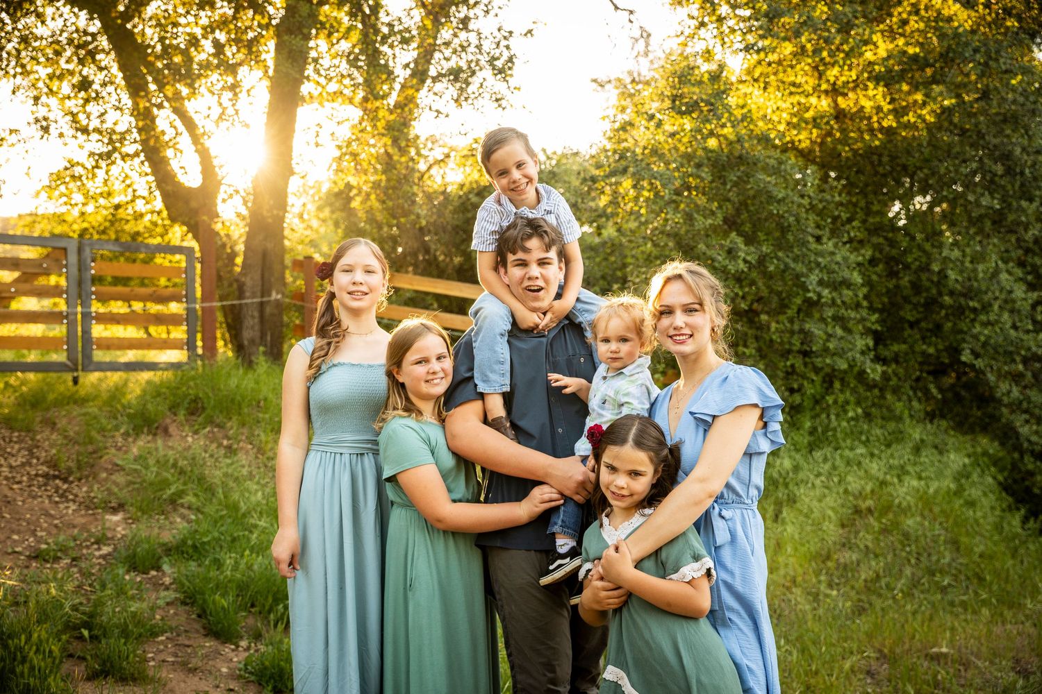 A family in coordinated outfits laughs together during a golden hour photoshoot in a park setting.