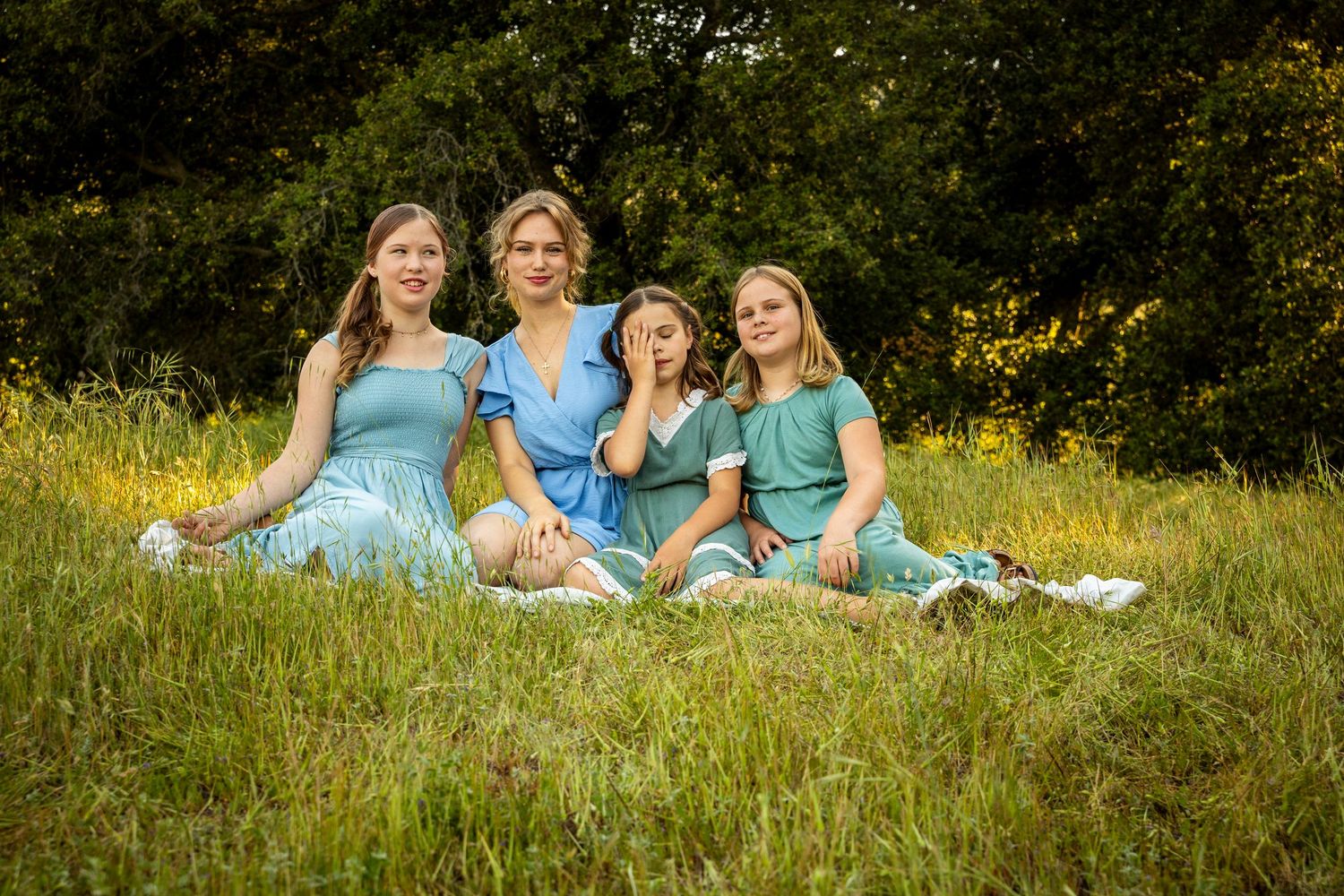 Family wearing coordinated blue outfits sitting together on a grassy hill during a summer photoshoot.