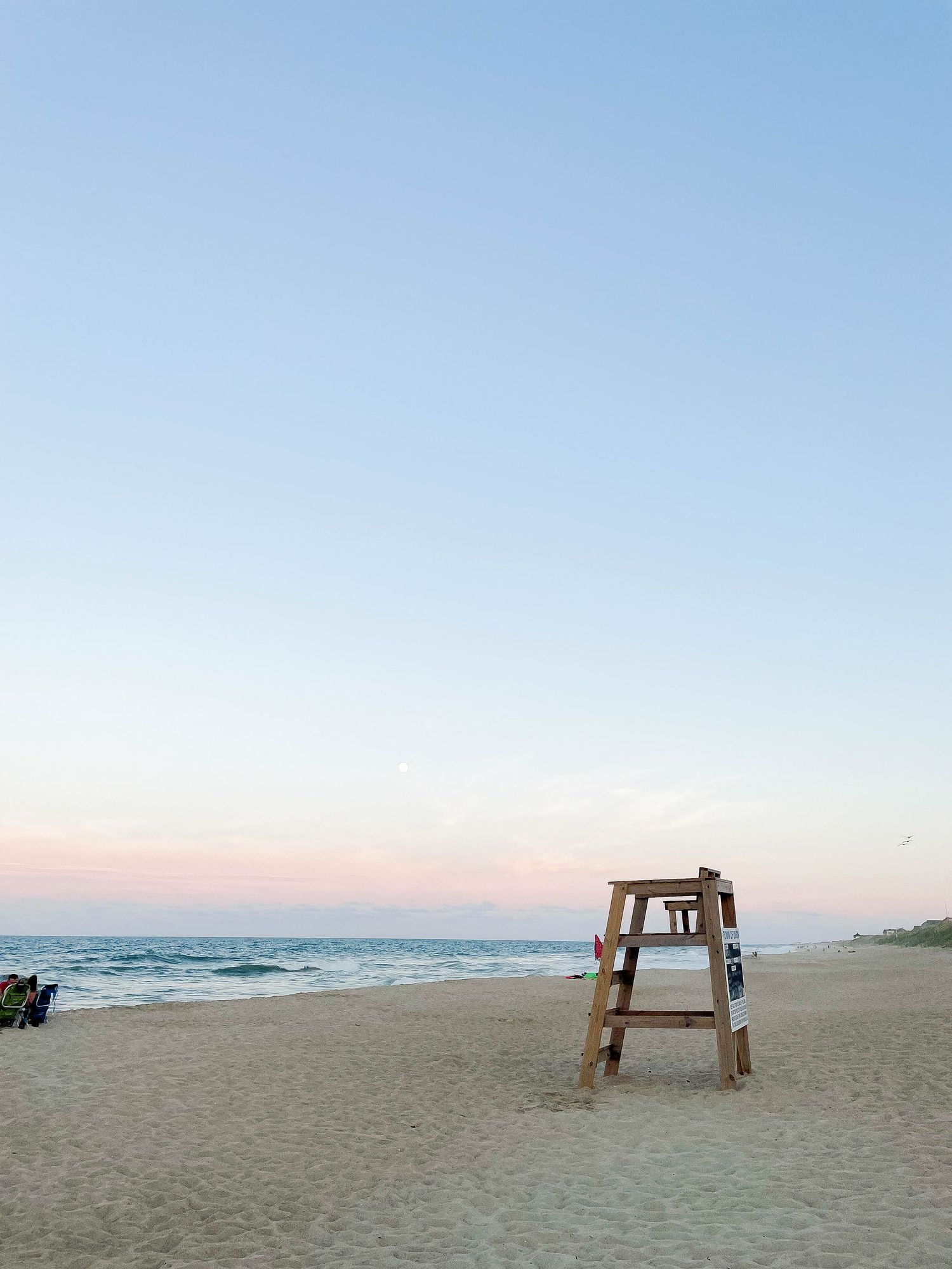 A row of beach lounge chairs facing the ocean at sunset creates a serene coastal setting.