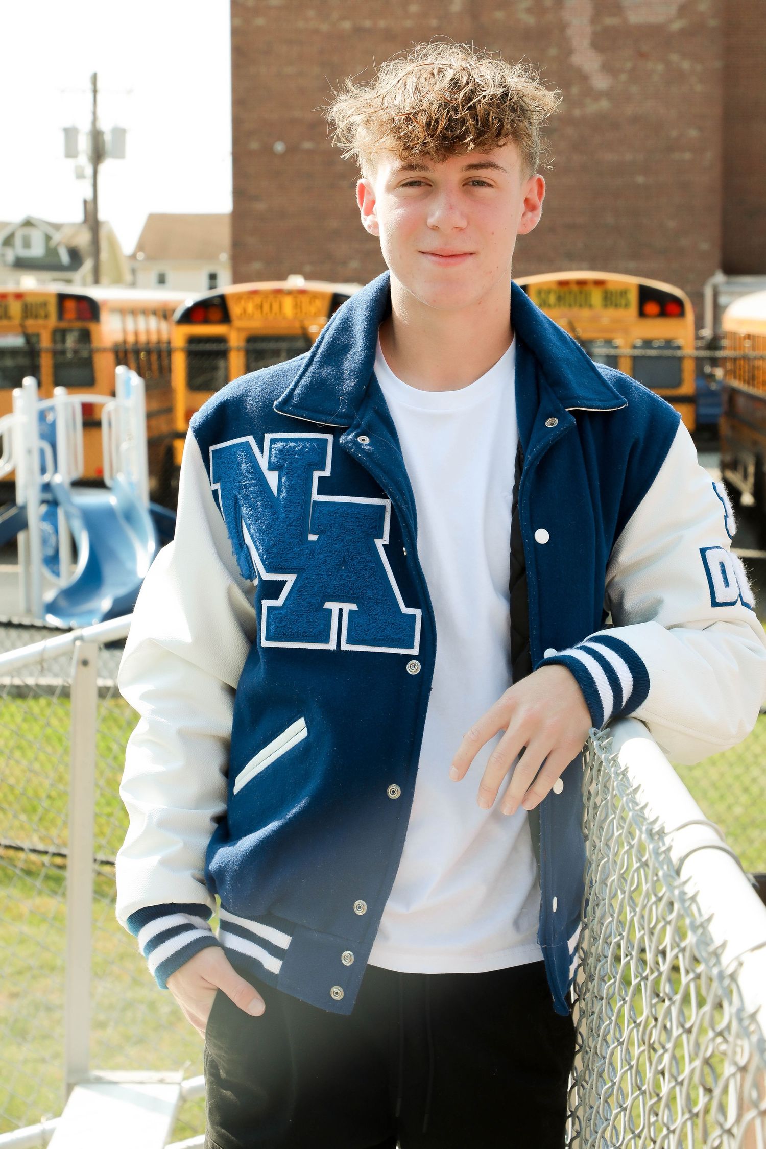 Outdoor portrait against chain link fence wearing blue and white varsity jacket.