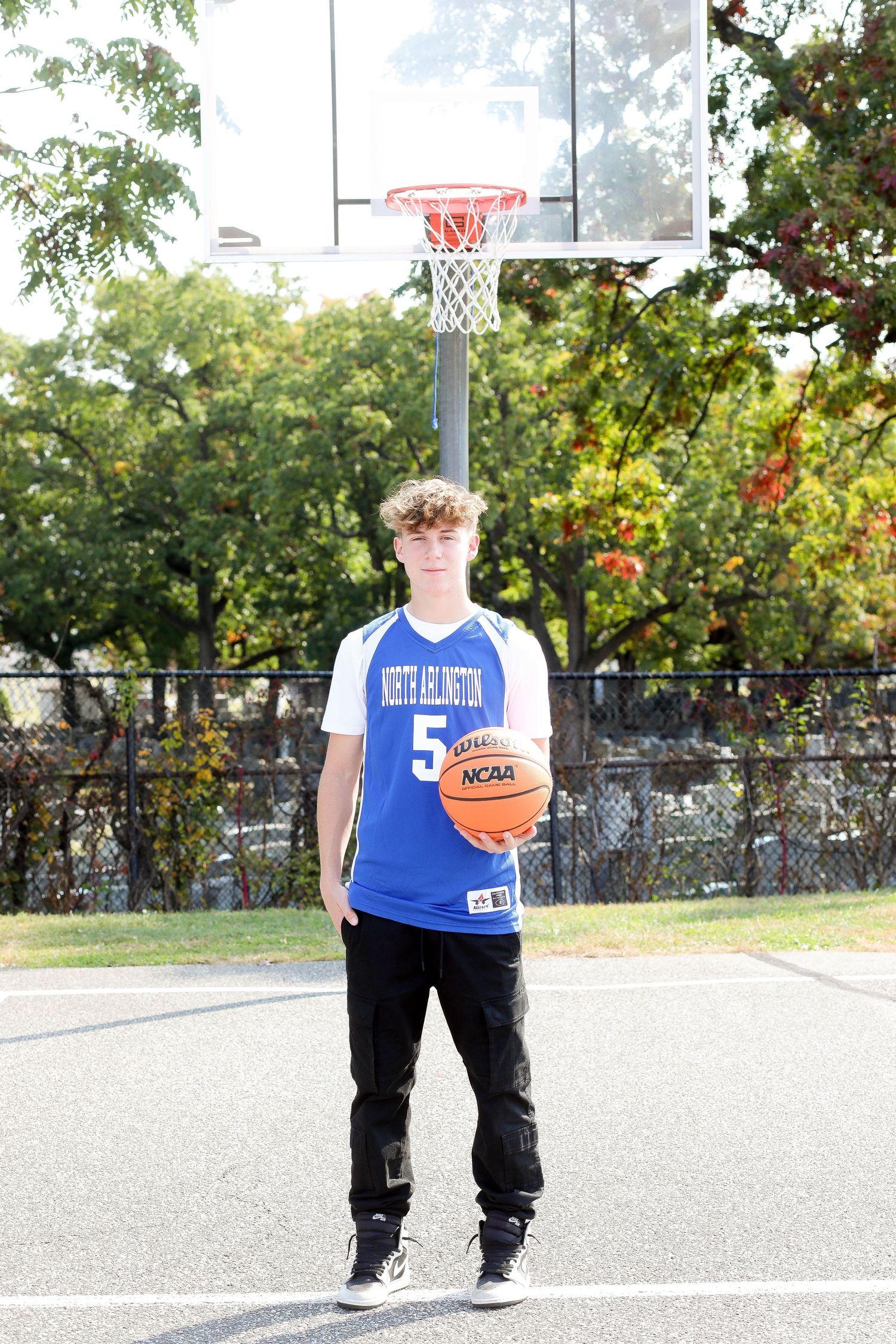 Basketball player in blue jersey number 5 poses with ball on outdoor court.