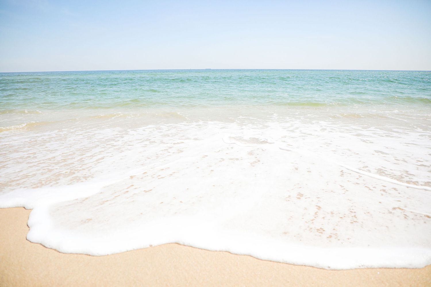 Turquoise ocean waves gently roll onto a pristine white sandy beach under bright blue skies.