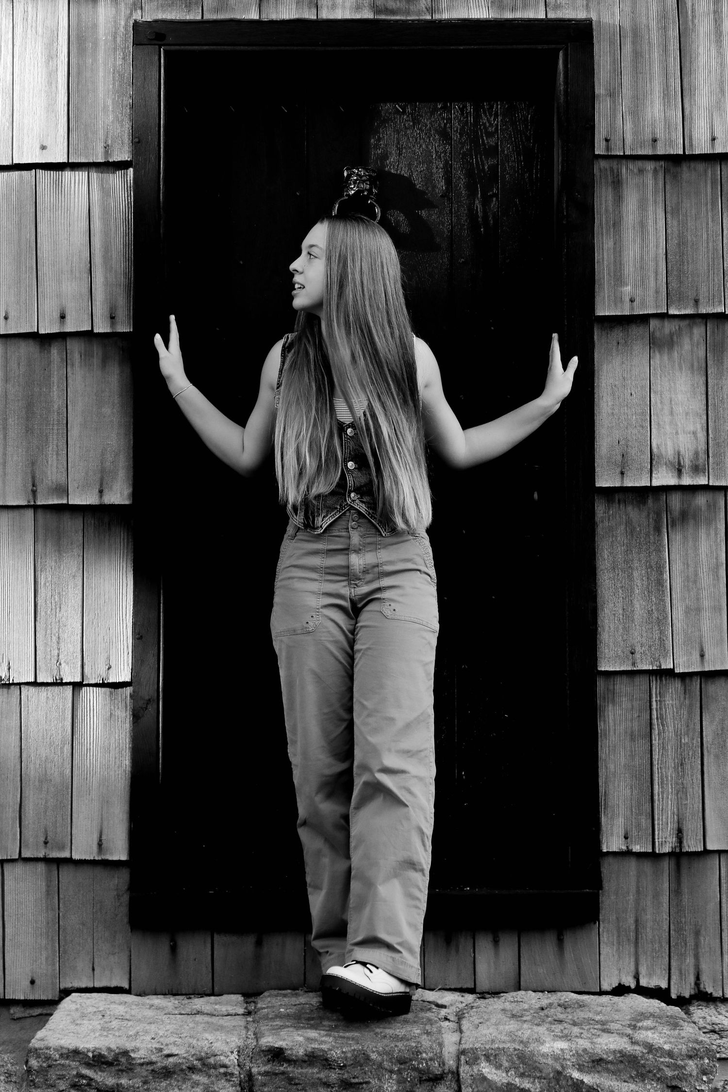 Black and white photo of a person posing against a dark doorway with wooden shingle siding.