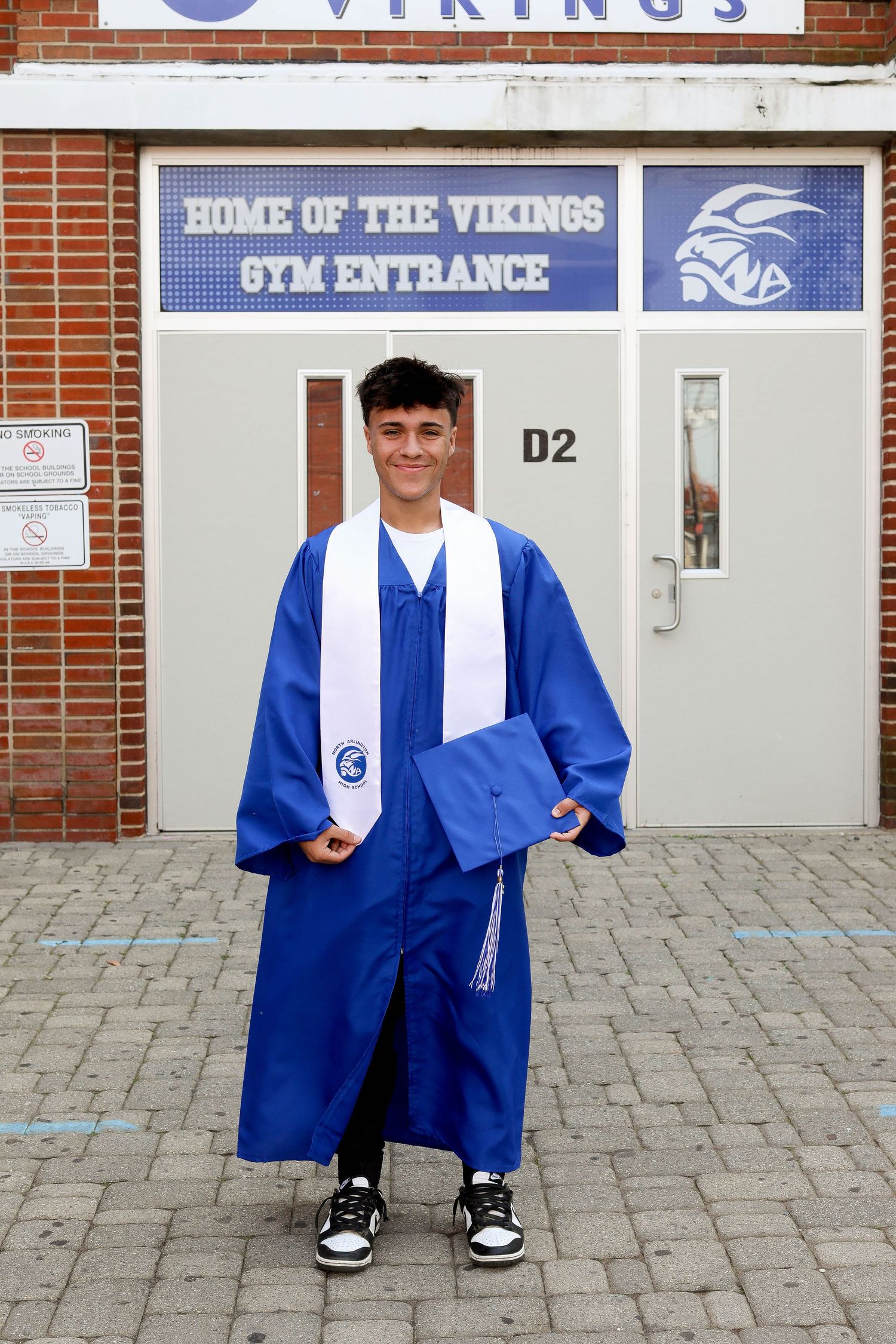 Student in graduation attire poses in front of North Arlington Vikings gym entrance.