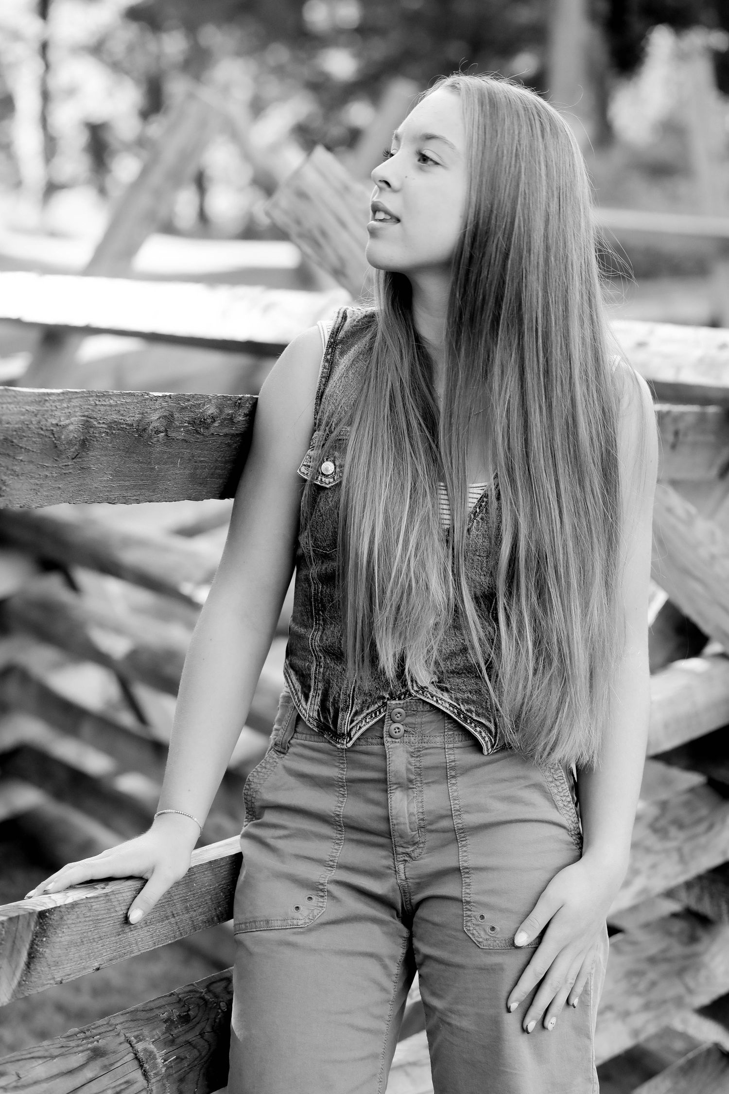Black and white portrait of a person sitting on wooden fencing outdoors.