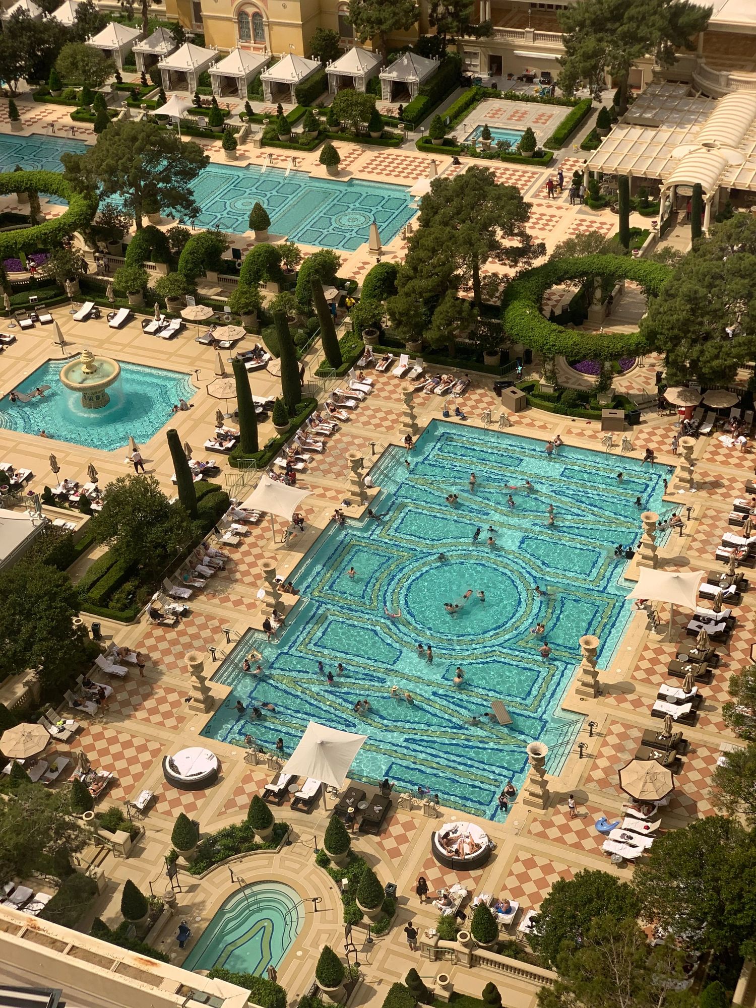 Aerial shots of a luxury resort swimming pool with geometric patterns and sunbathers lounging on the pool deck on a sunny day.