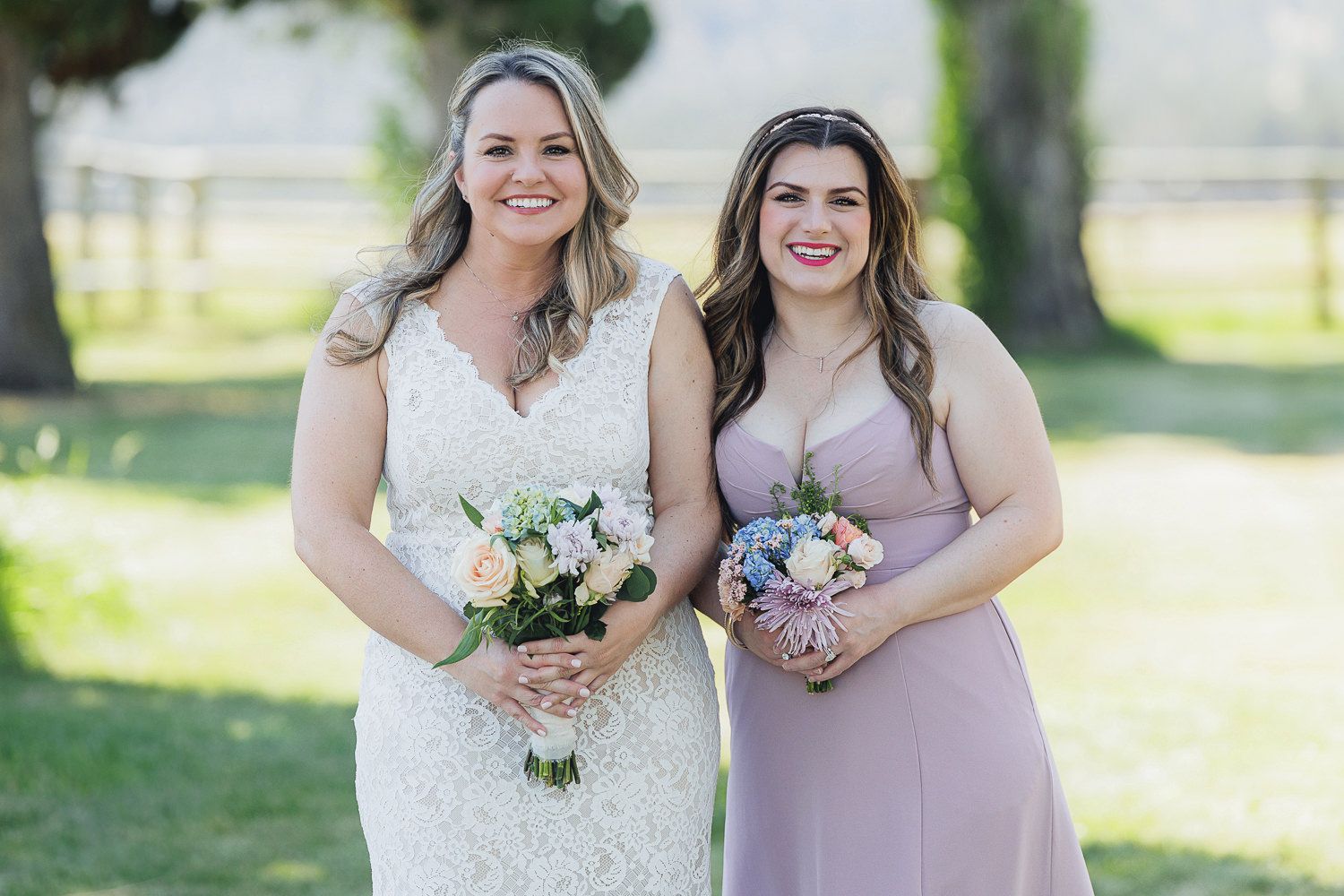 Bridesmaids in lavender dresses hold white floral bouquets while standing outdoors on a sunny day.