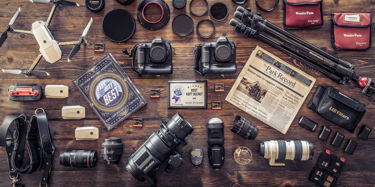 Flat lay of professional photography equipment including cameras, lenses and accessories on wooden surface.
