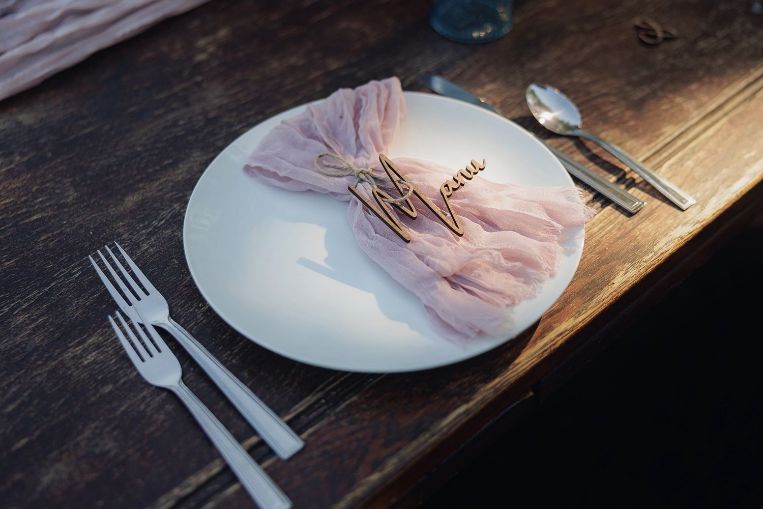 Light pink napkin elegantly folded with delicate twig decoration on white plate against rustic wooden table.